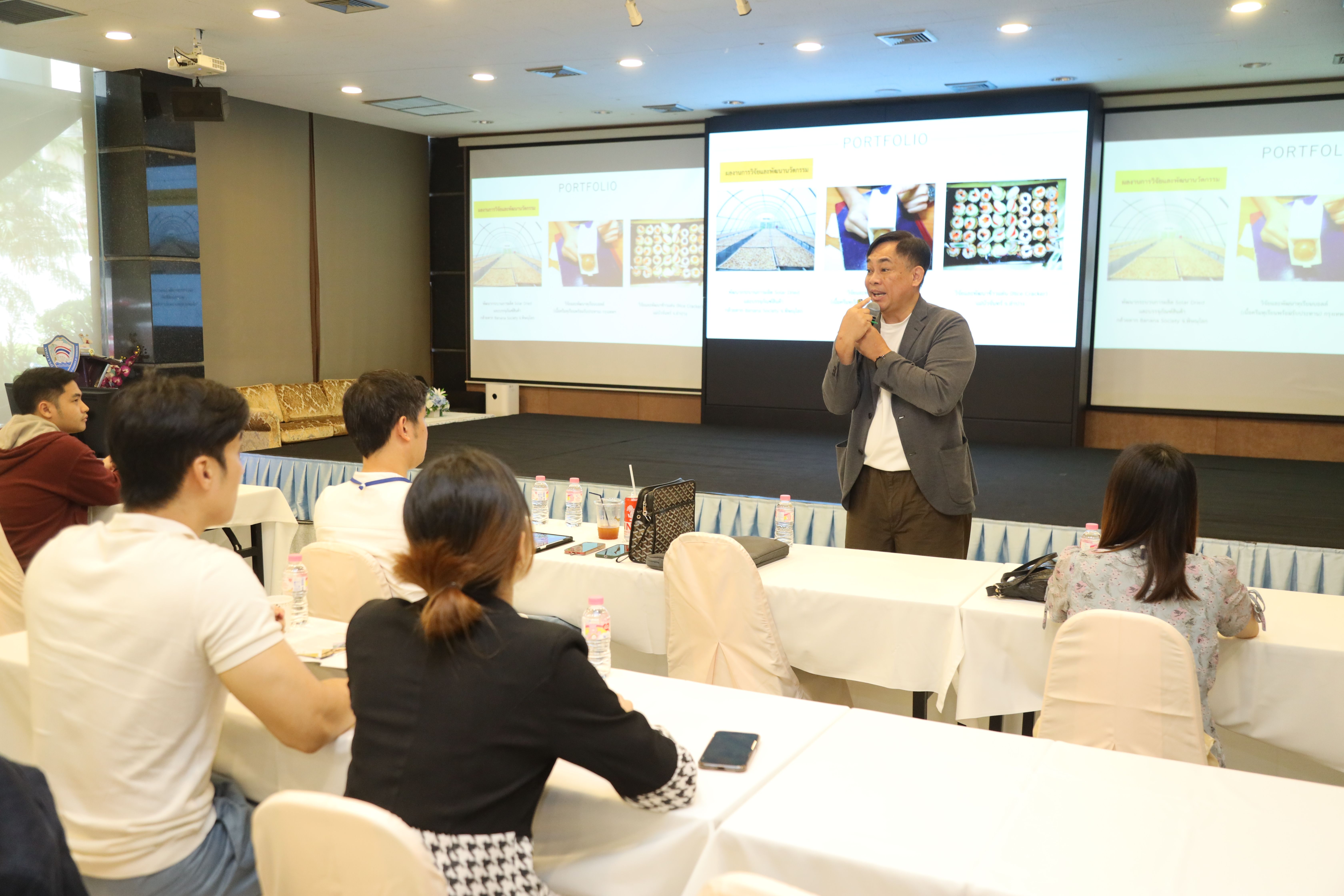 A man presents to an audience in a conference room with slides on a projector.
