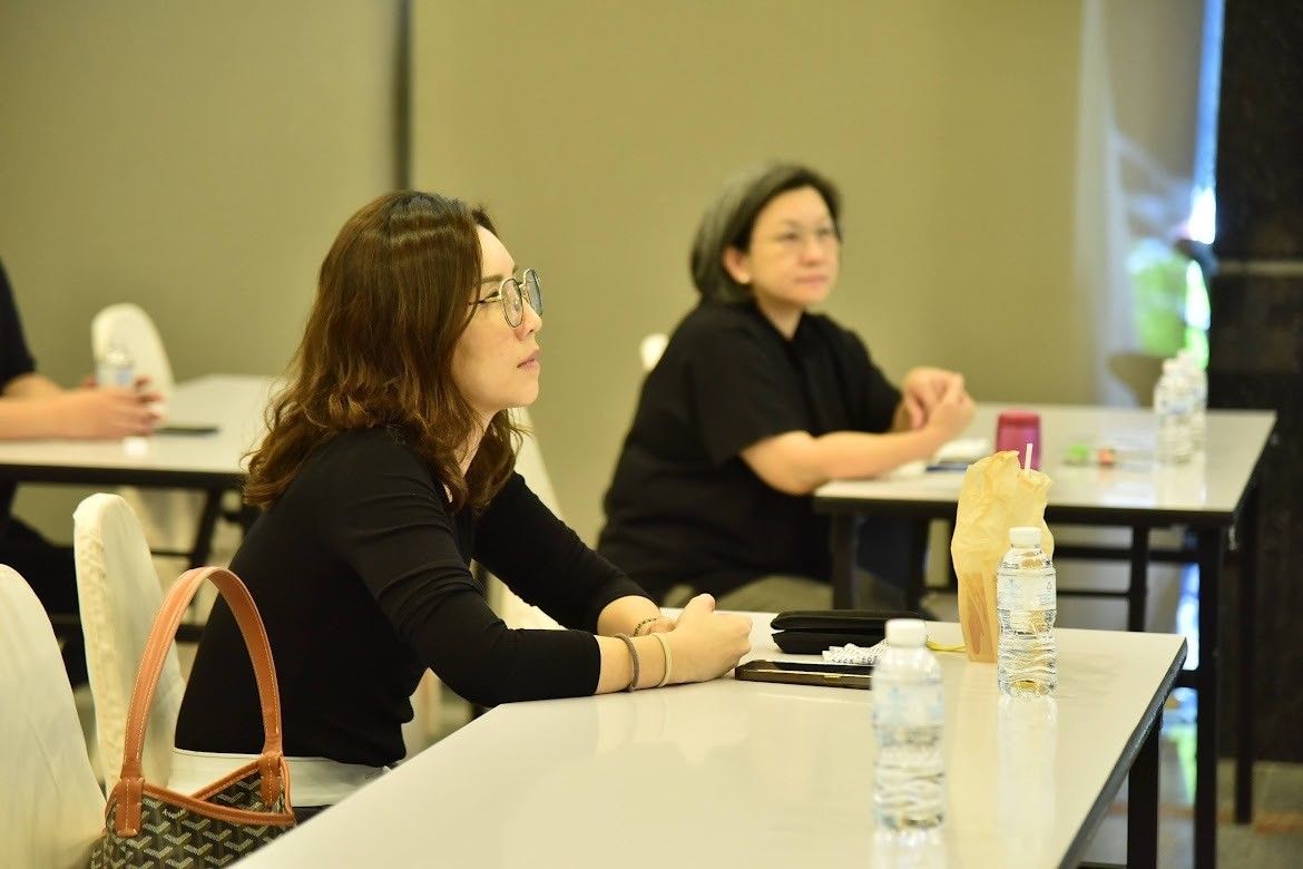 Woman with glasses and dark top listening intently at a conference.
