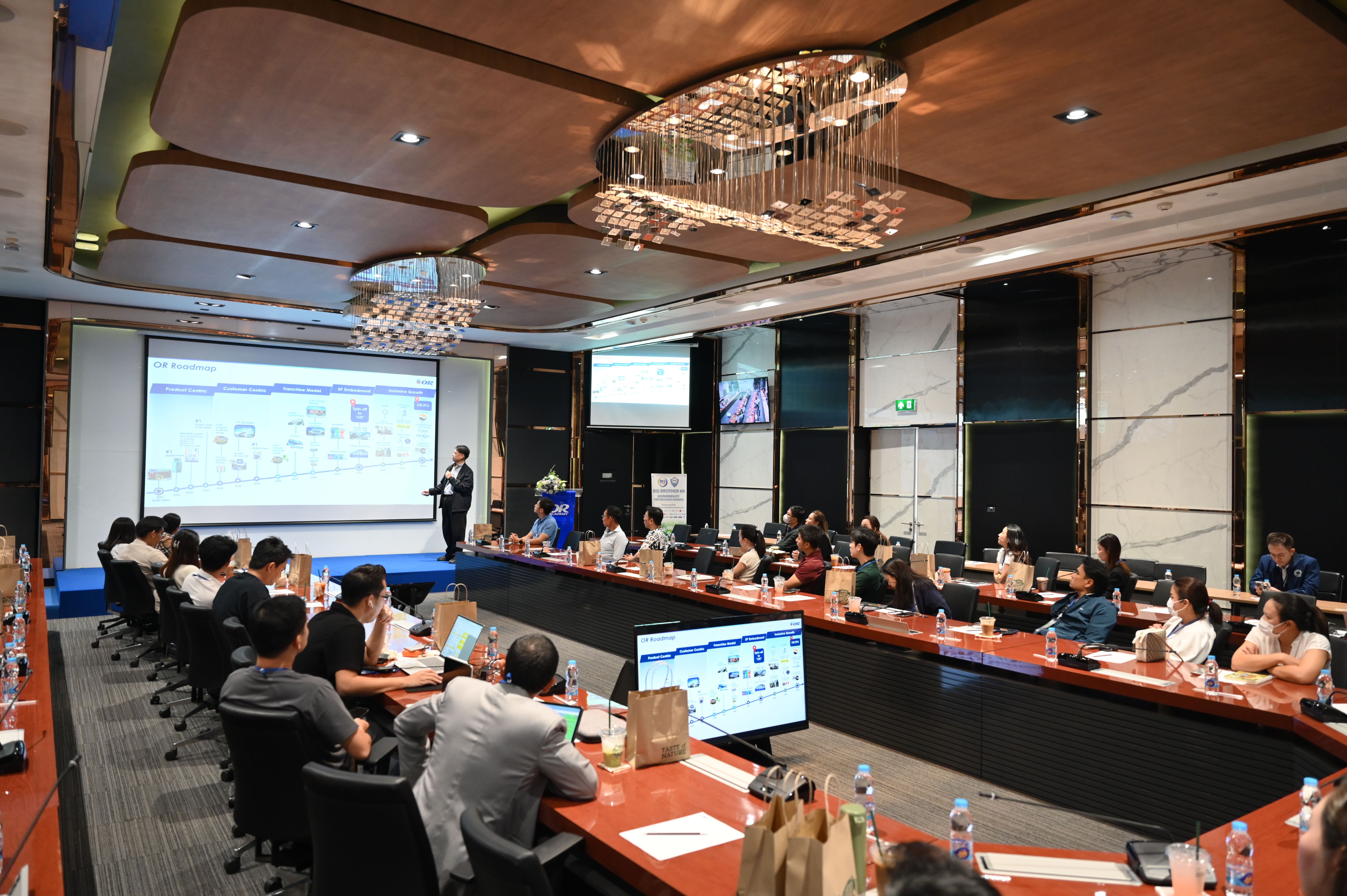 Attendees at a conference watch a presenter on a large screen displaying a diagram.