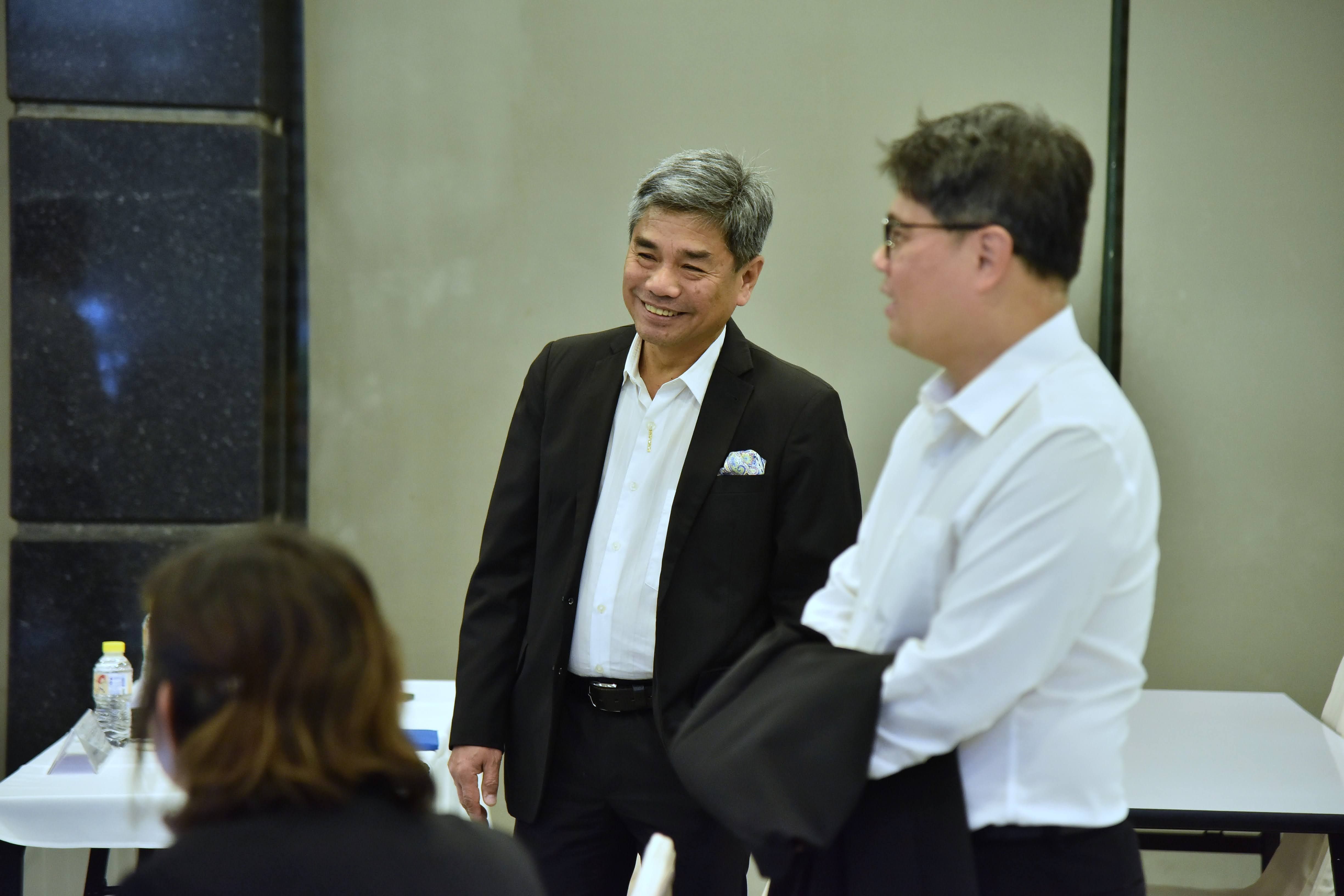 Two men, one in a suit and one in a white shirt, conversing in a meeting room.