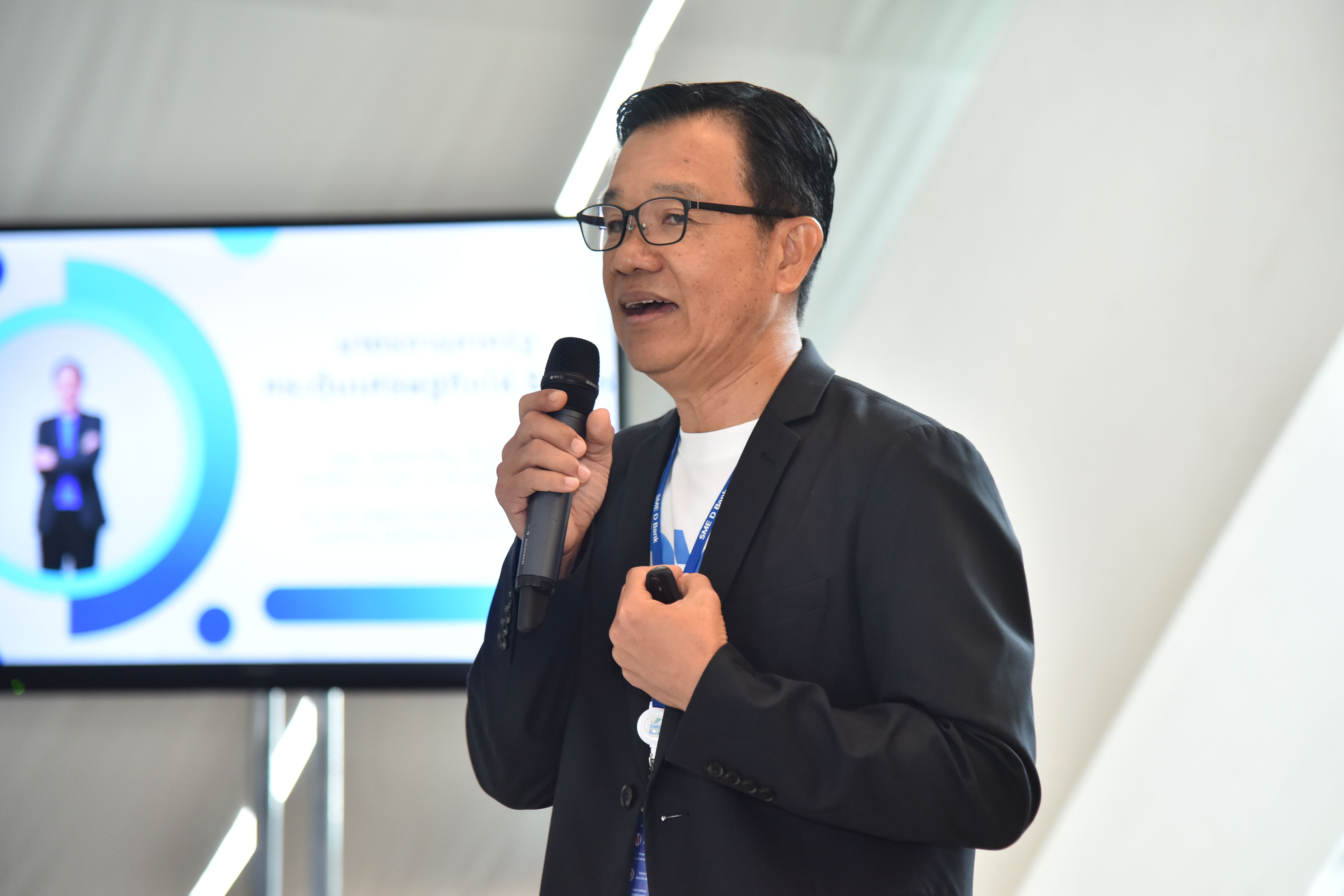 Man in glasses speaking into a microphone during a presentation.
