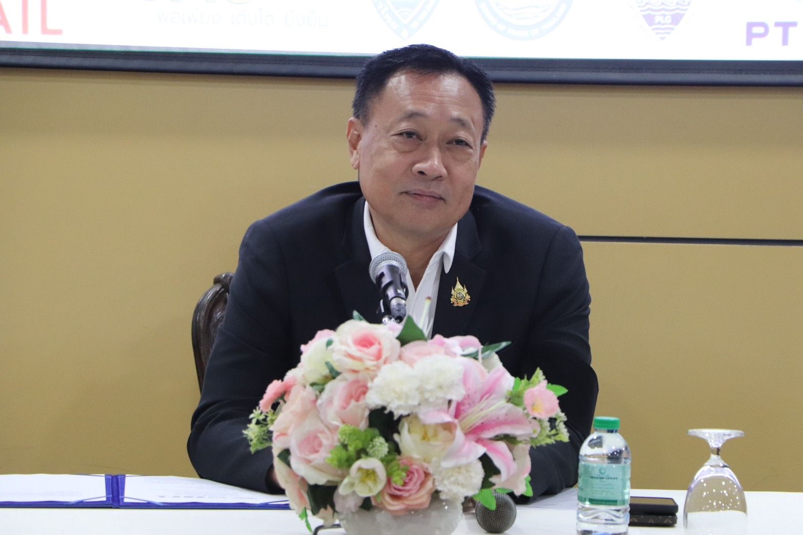 Man in dark suit sitting at a table with a floral centerpiece.