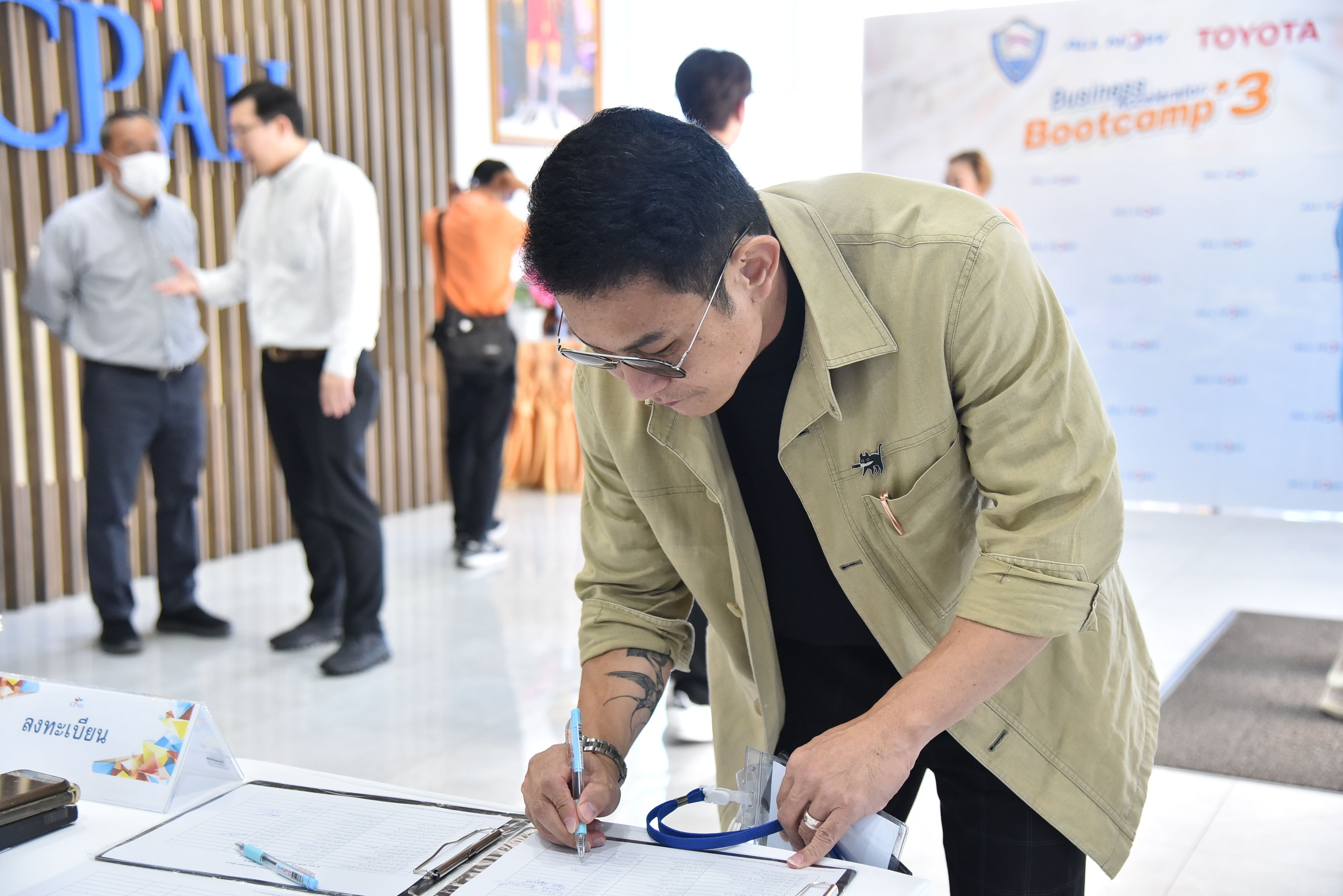 Man in light brown jacket signs a document at a registration table.