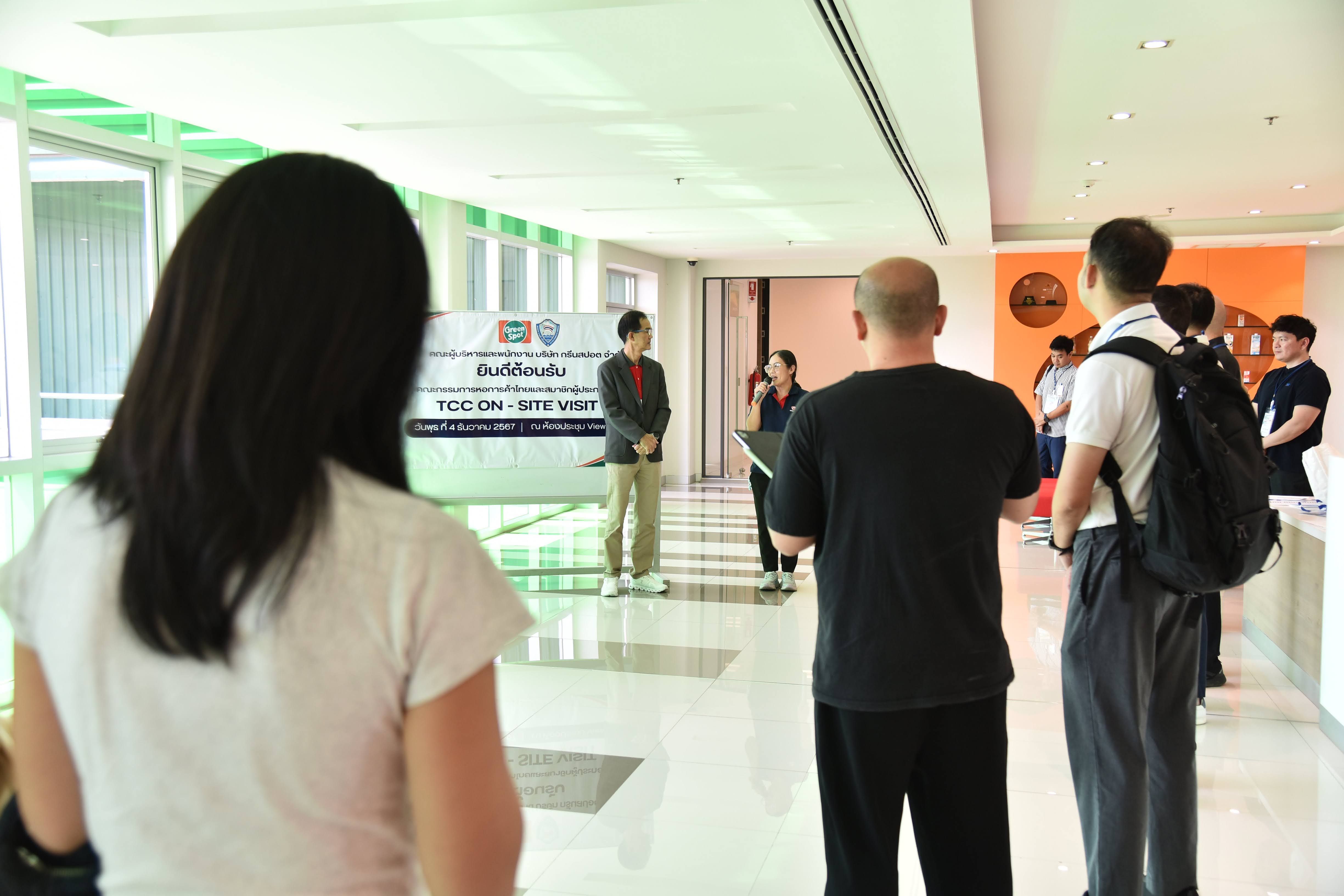 People gather in a bright, modern hallway, observing a banner and a speaker.