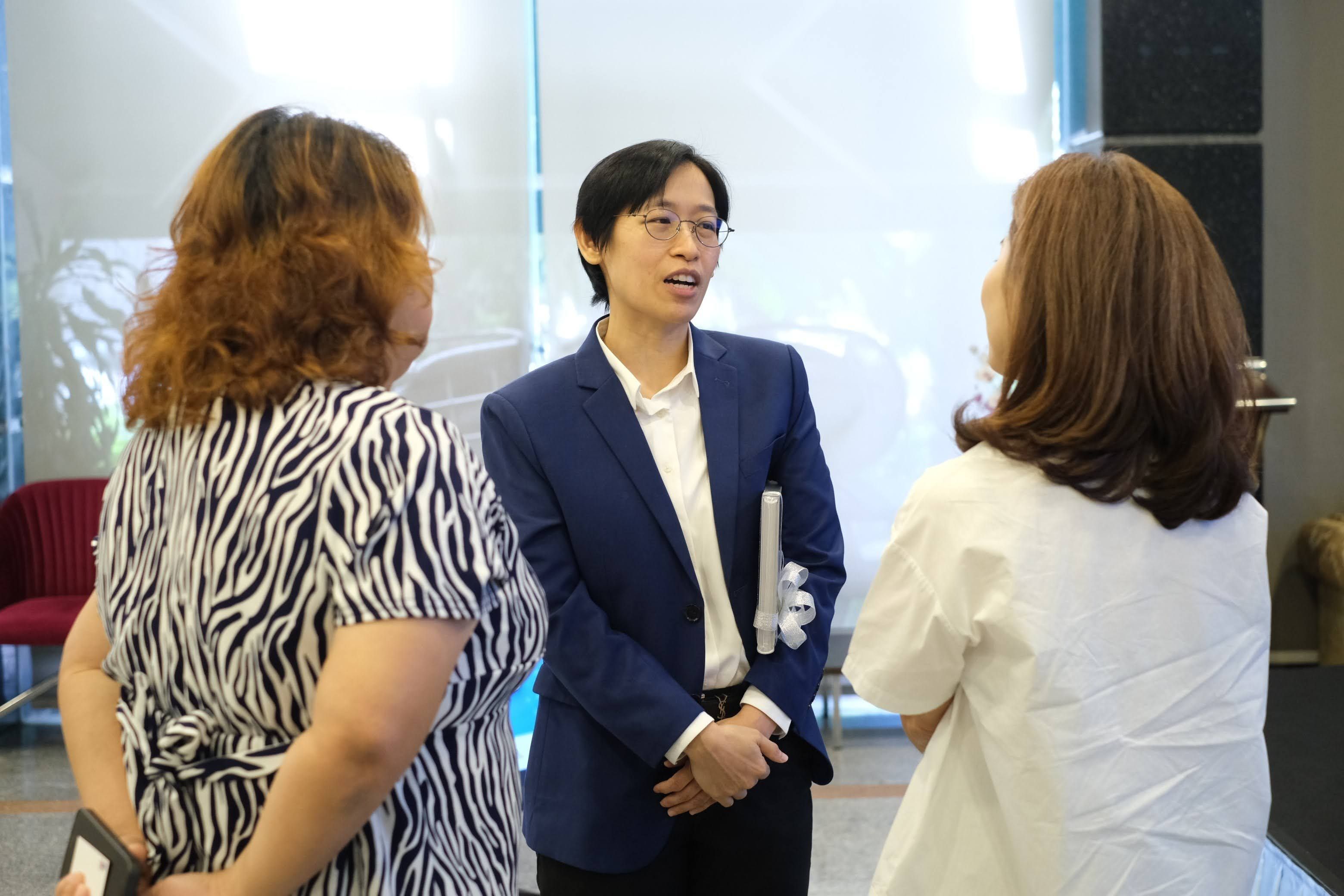 Three people, including one in a blue suit, engaged in a professional conversation indoors.