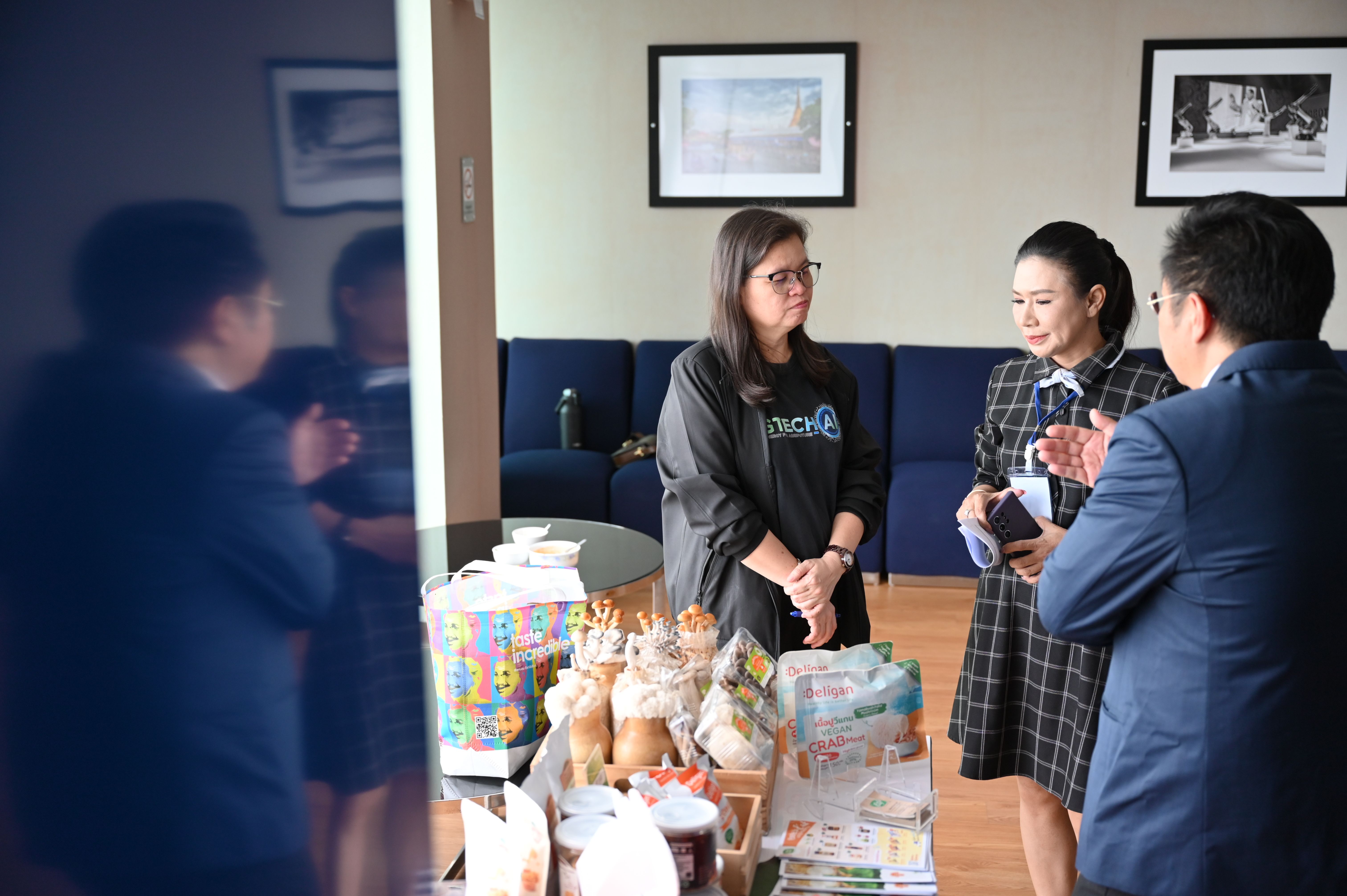 Three people interacting around a table with gifts and souvenirs in an office setting.