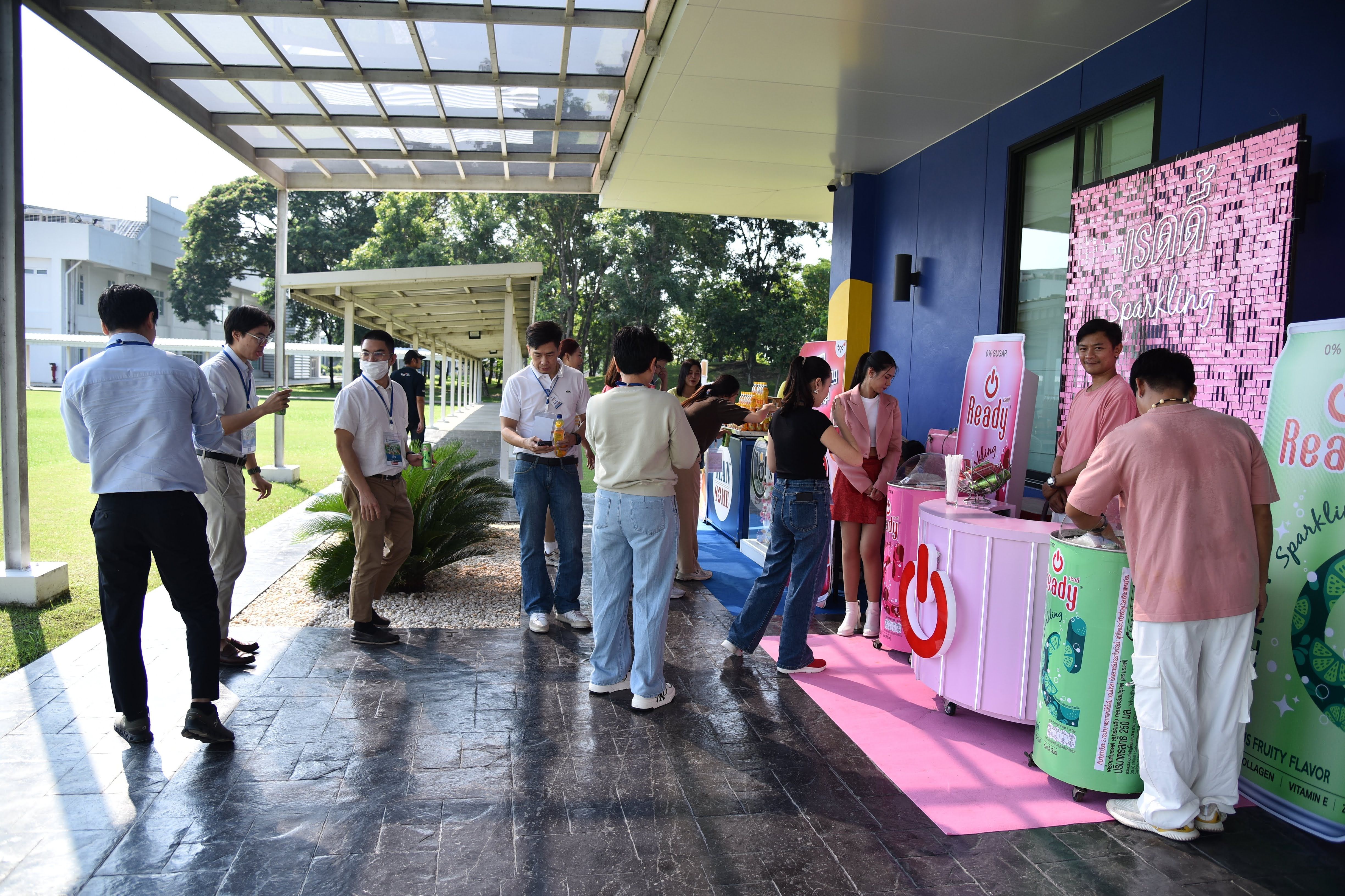 Young adults gather at an outdoor event booth with pink decorations and refreshments.