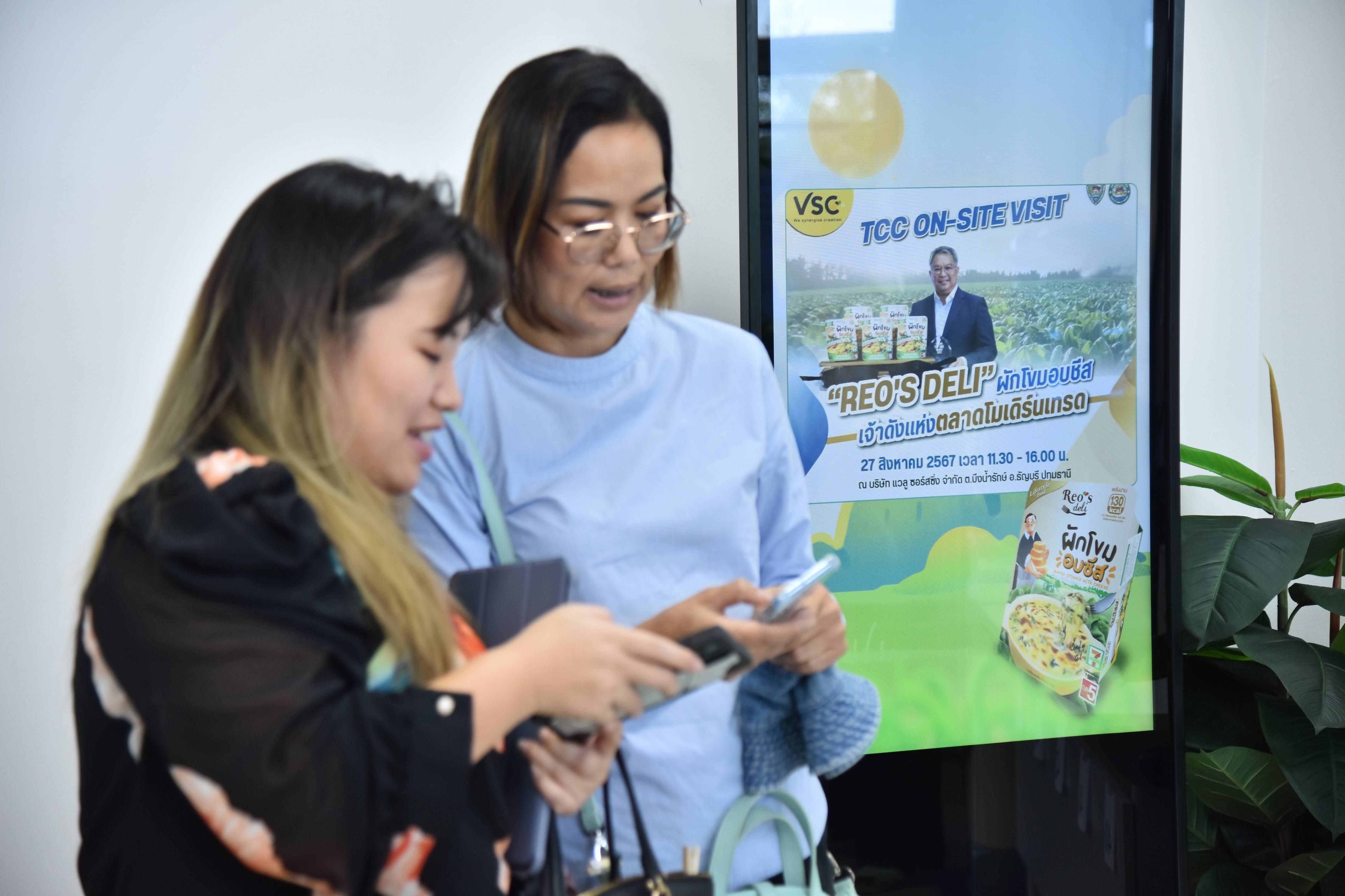 Two women engaging with a mobile device near a digital advertising screen.
