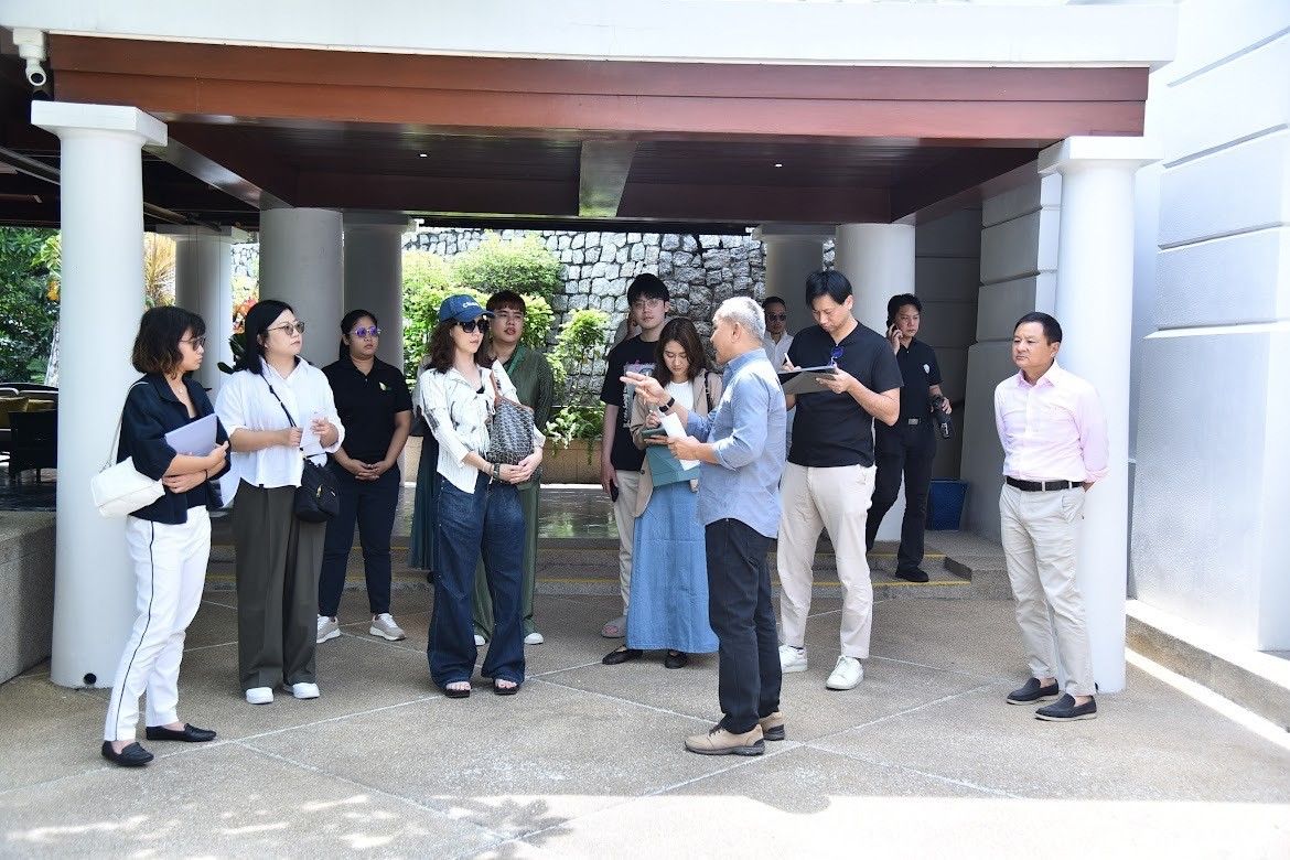 A diverse group of adults gathers outdoors under a modern building's sheltered entrance.