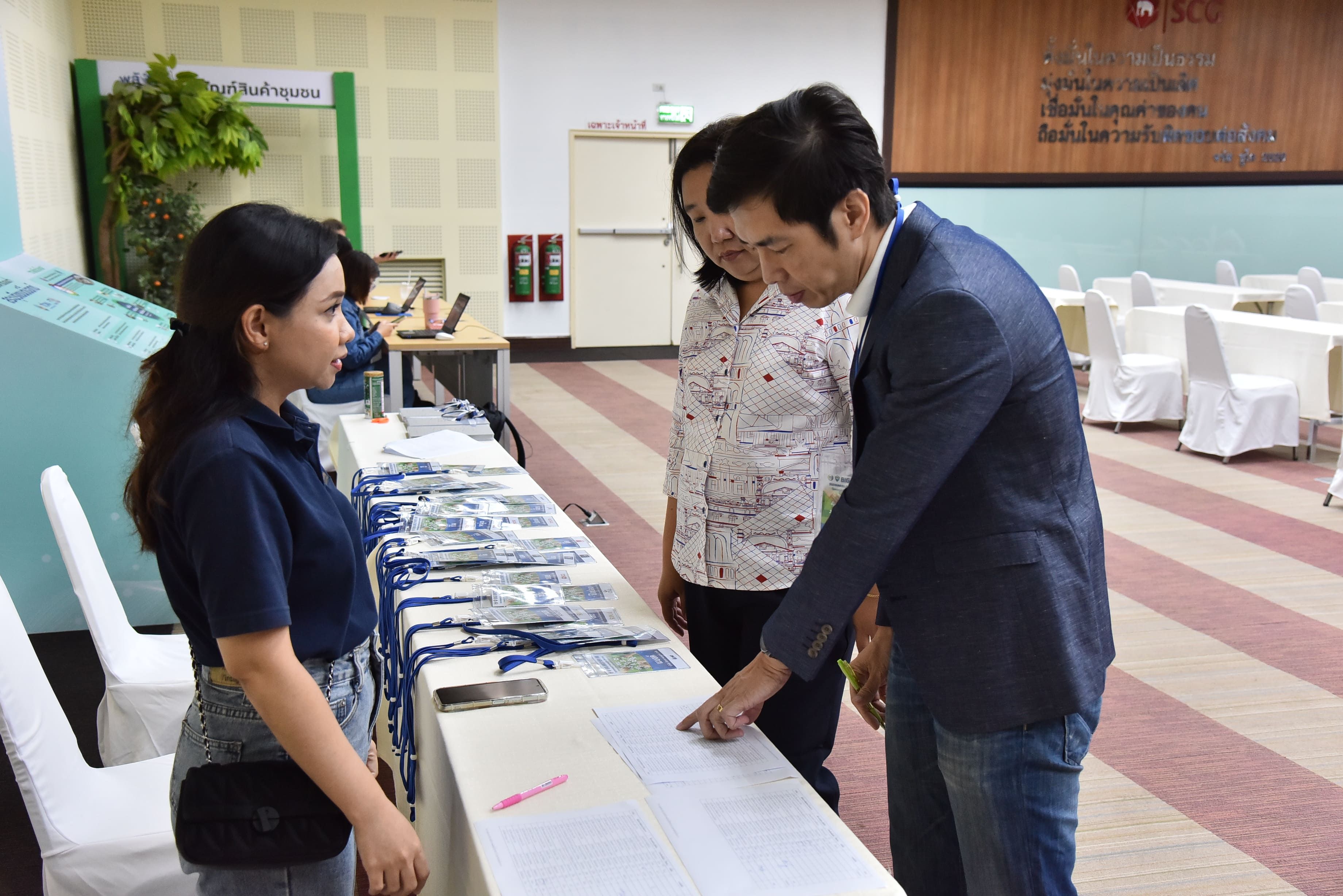 Man points at documents on table, two women observe at an event.