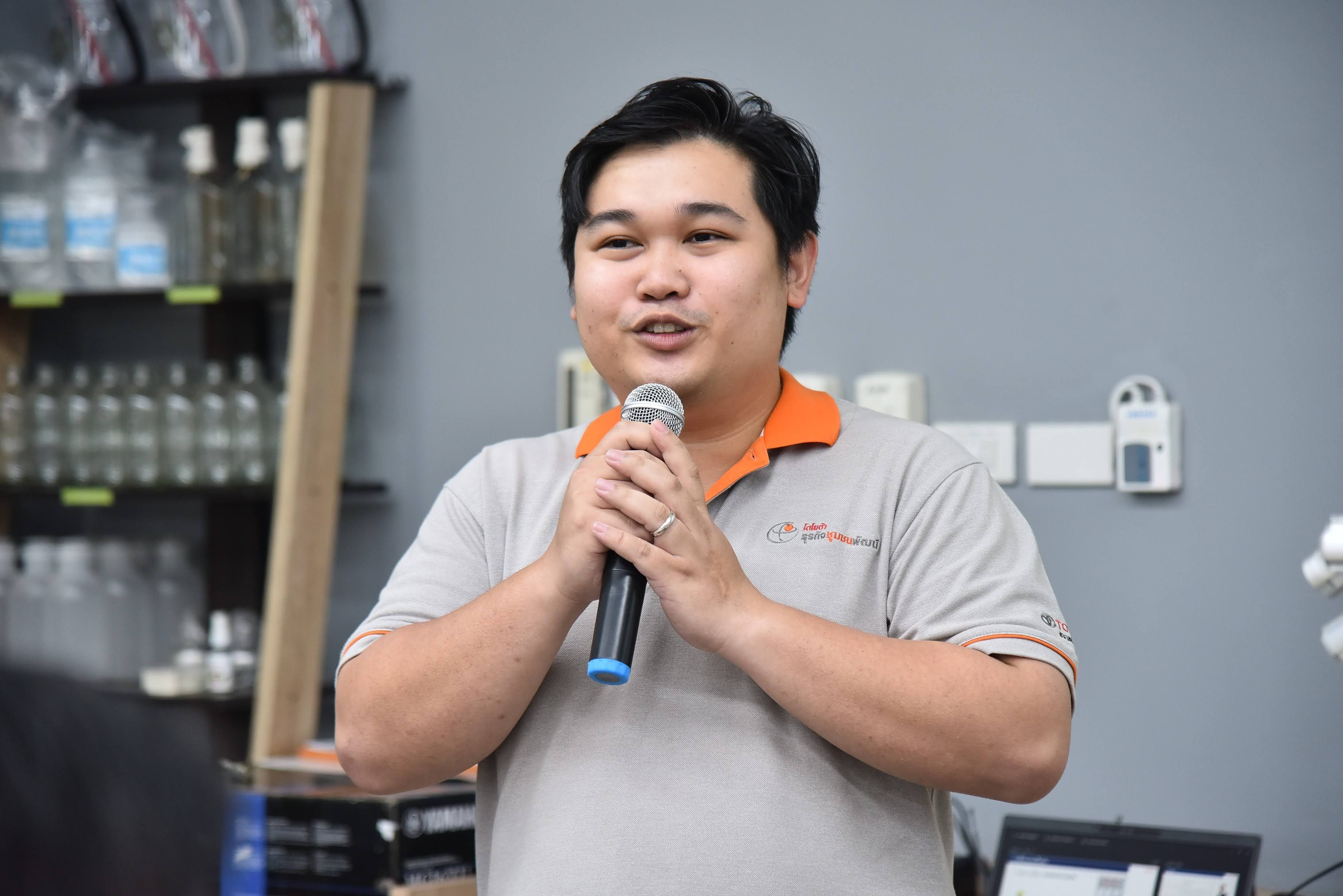 A man in a polo shirt speaks into a microphone during a presentation.
