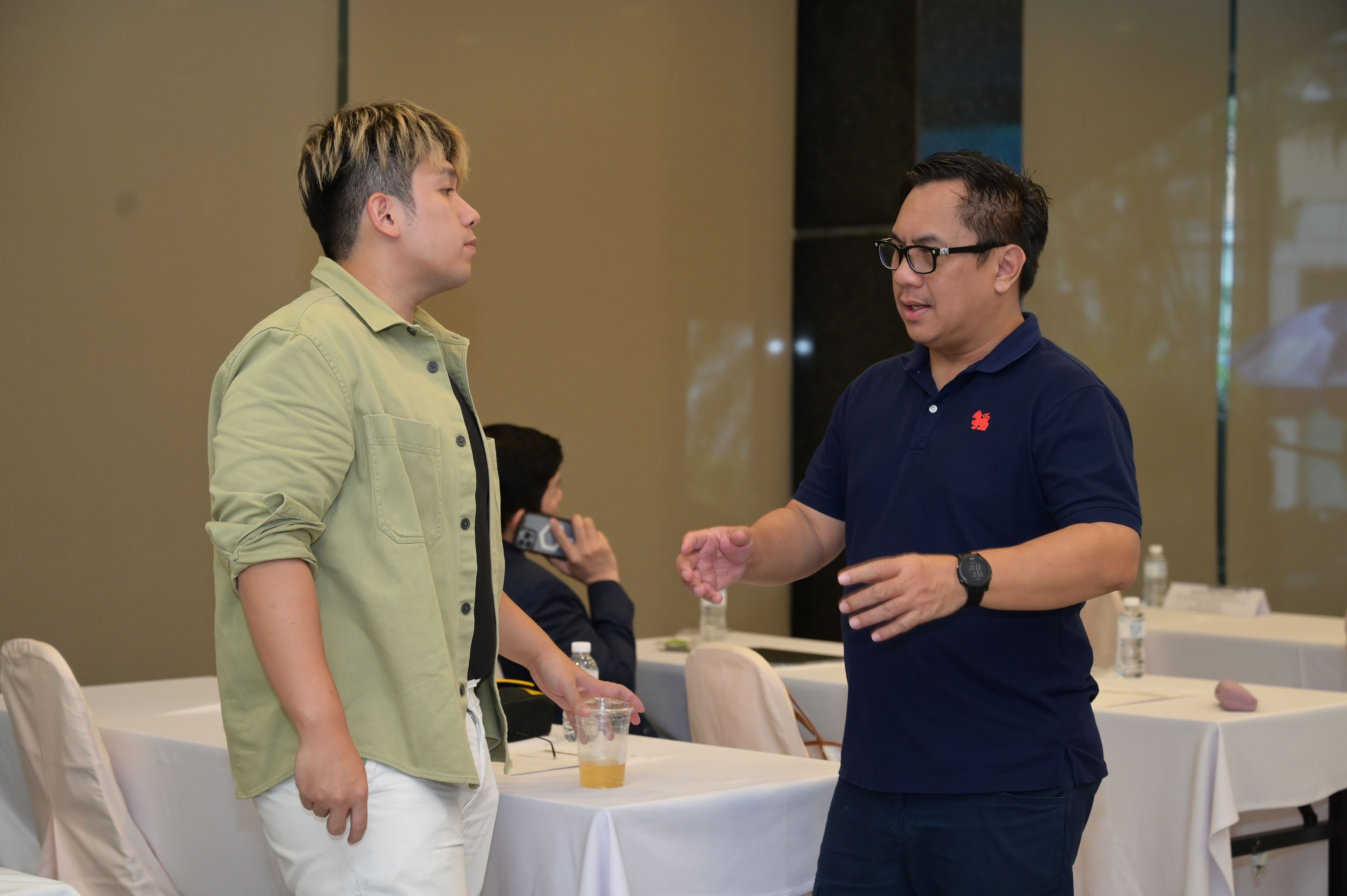 Two men in a room are engaged in conversation, one wearing a green shirt.