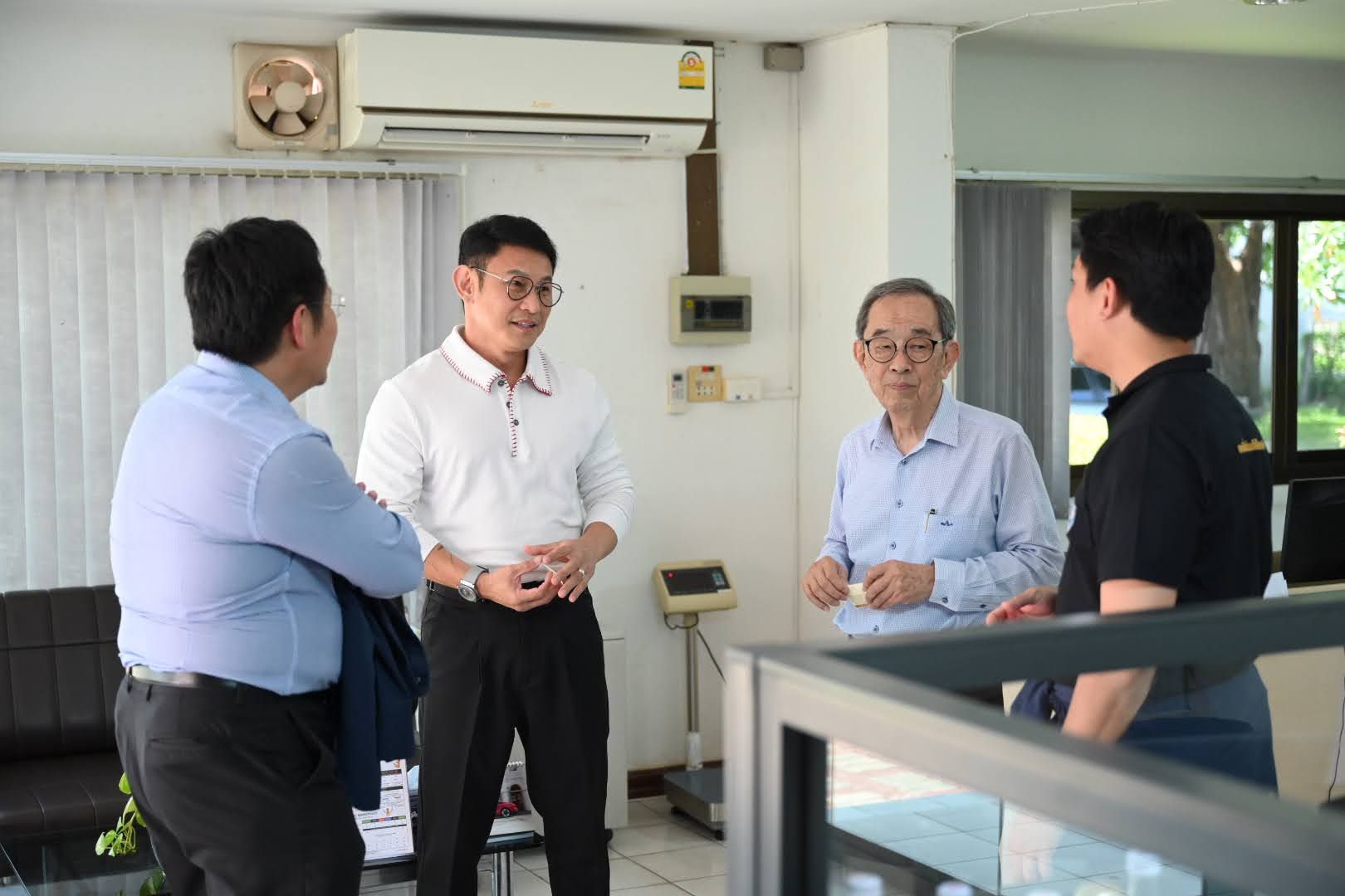 Four men converse in a brightly lit office, one gesturing animatedly.