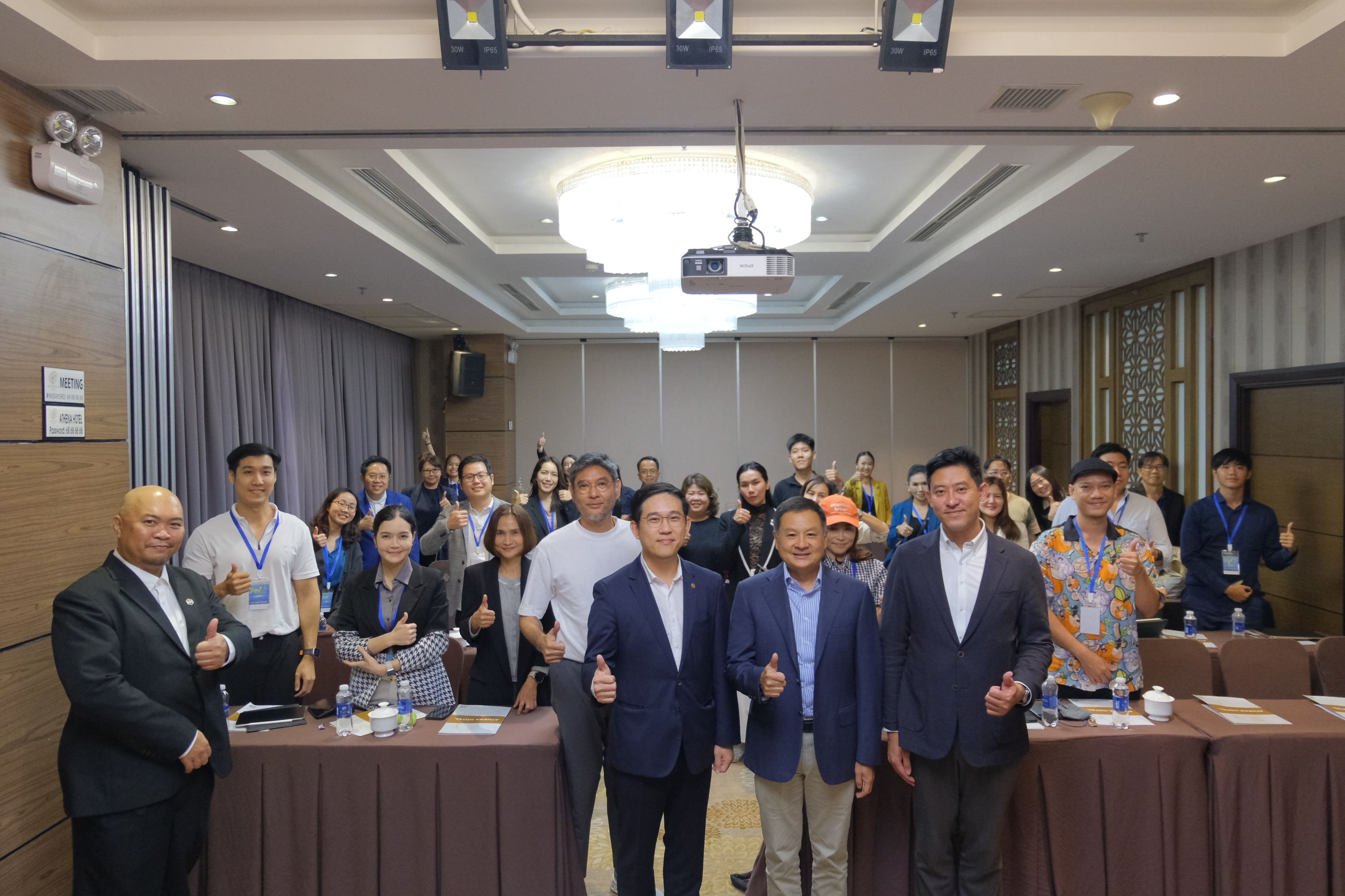 A large group of professionals smiling in a modern conference room, some giving thumbs up.