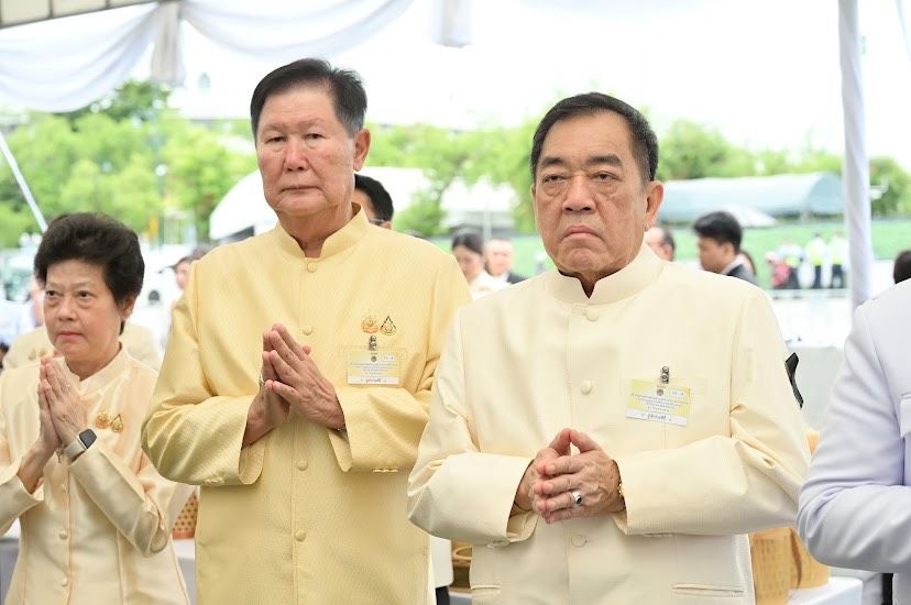 Two Thai men and a woman in traditional attire perform a respectful 'wai' gesture.