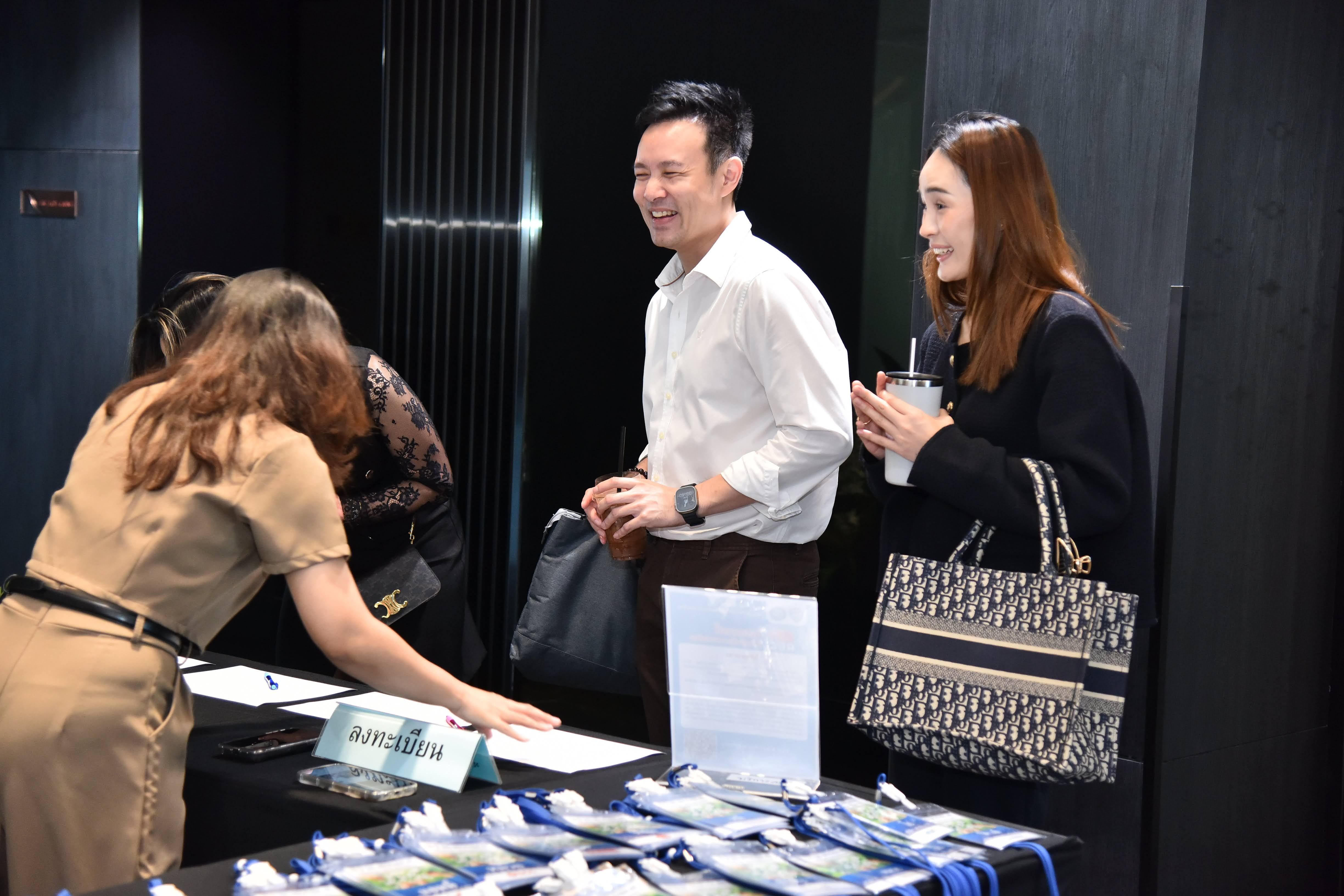 Woman assists smiling attendees at an event registration table with lanyards.