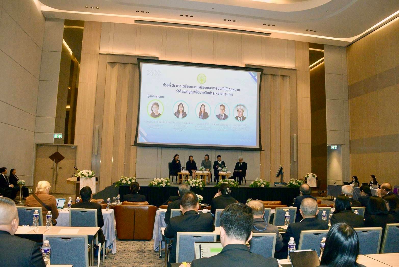 Panelists present on stage to a large audience at a formal conference.