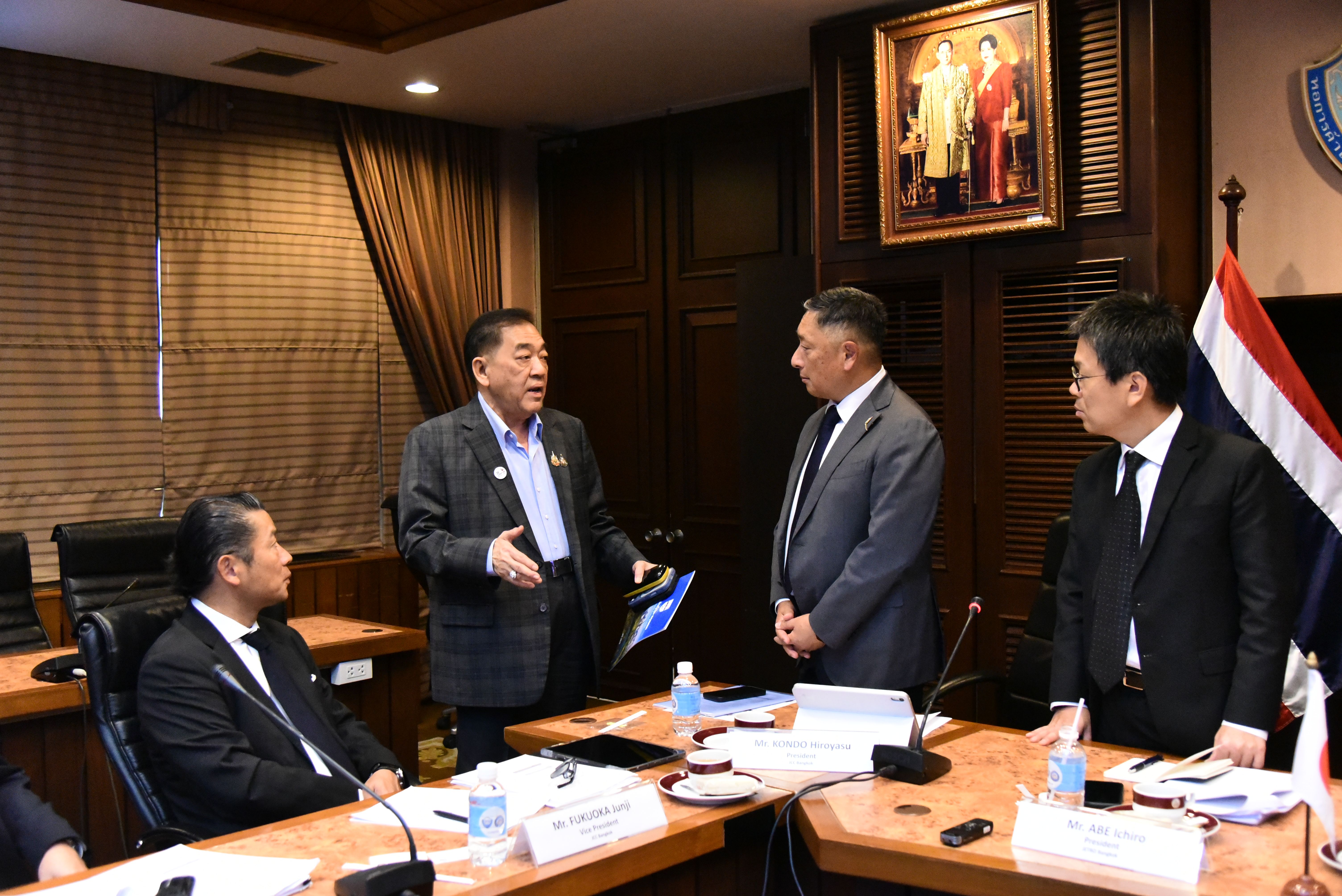 Four men in suits conduct a formal meeting around a dark conference table.