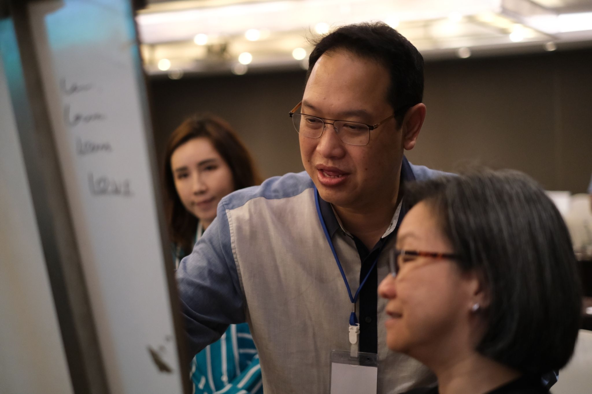 Man in glasses discusses content on a whiteboard with a woman in a professional setting.