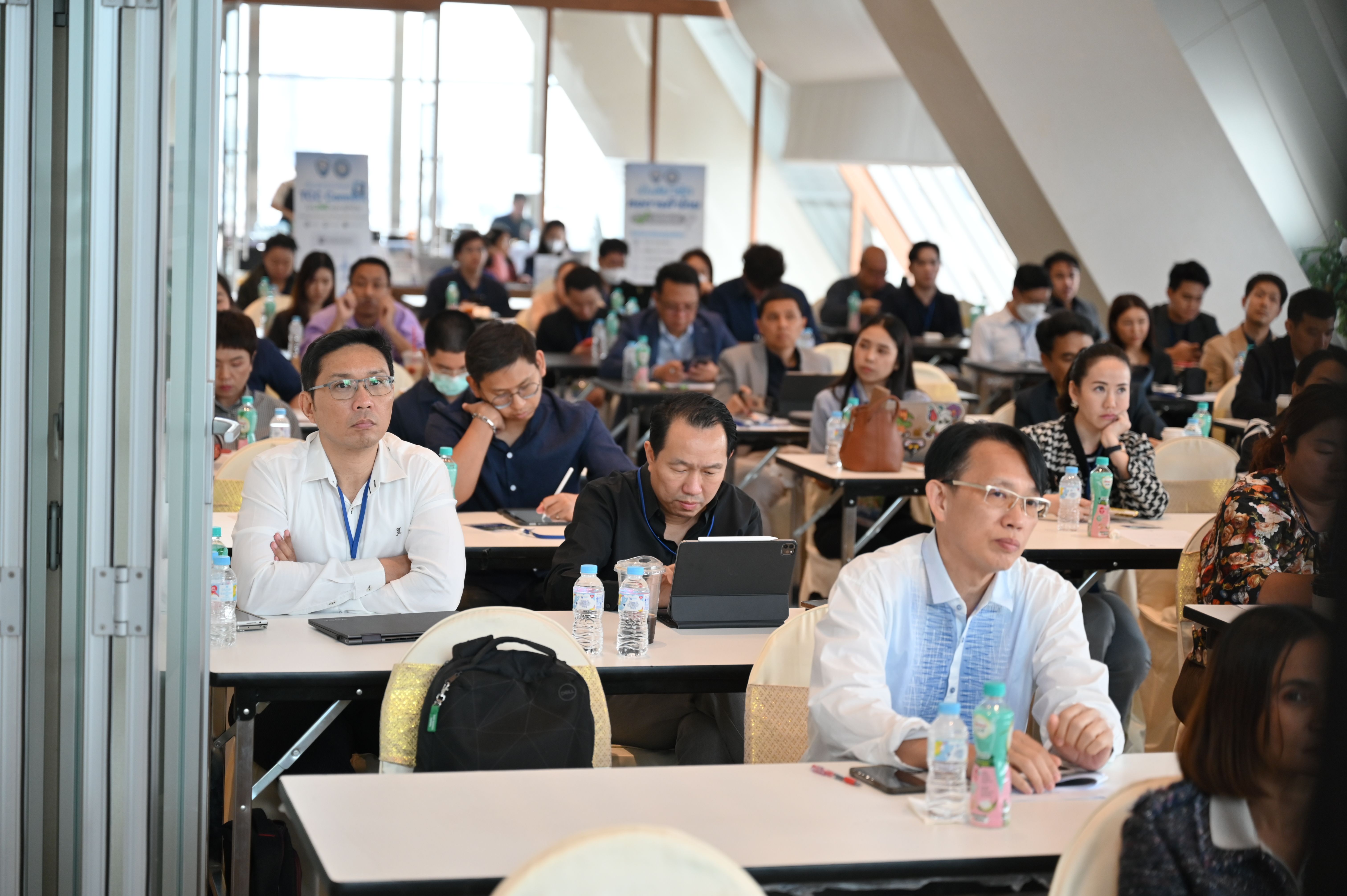 Attendees listening attentively at a business conference, with laptops and notebooks on tables.