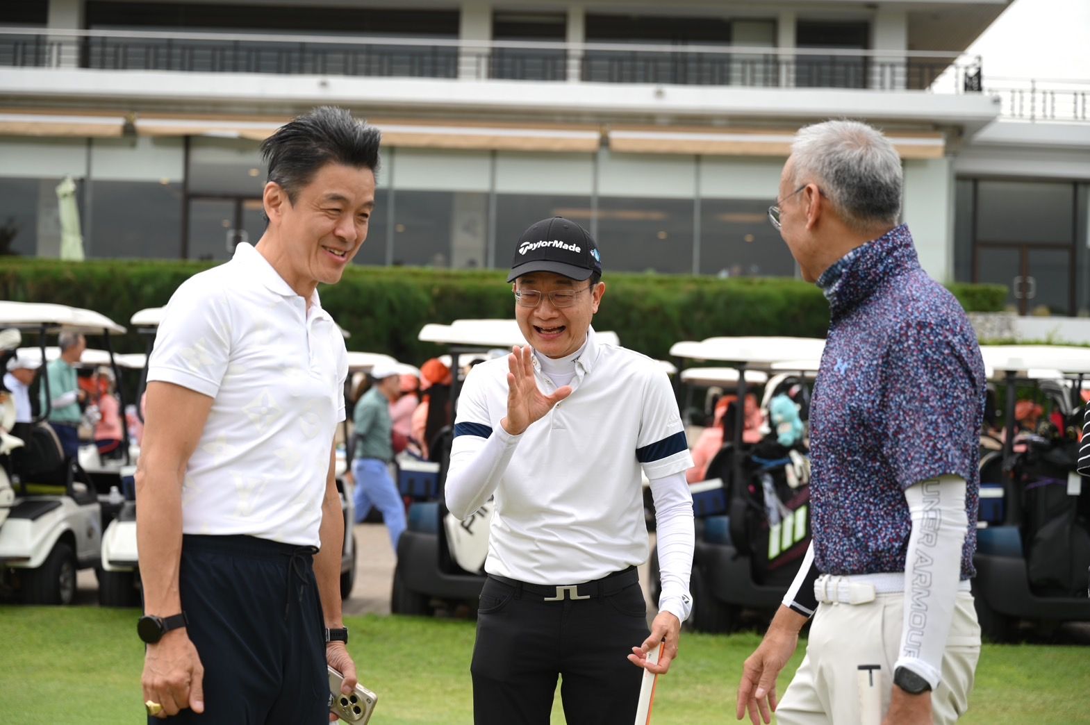 Three men in golf attire laugh and converse on a golf course.