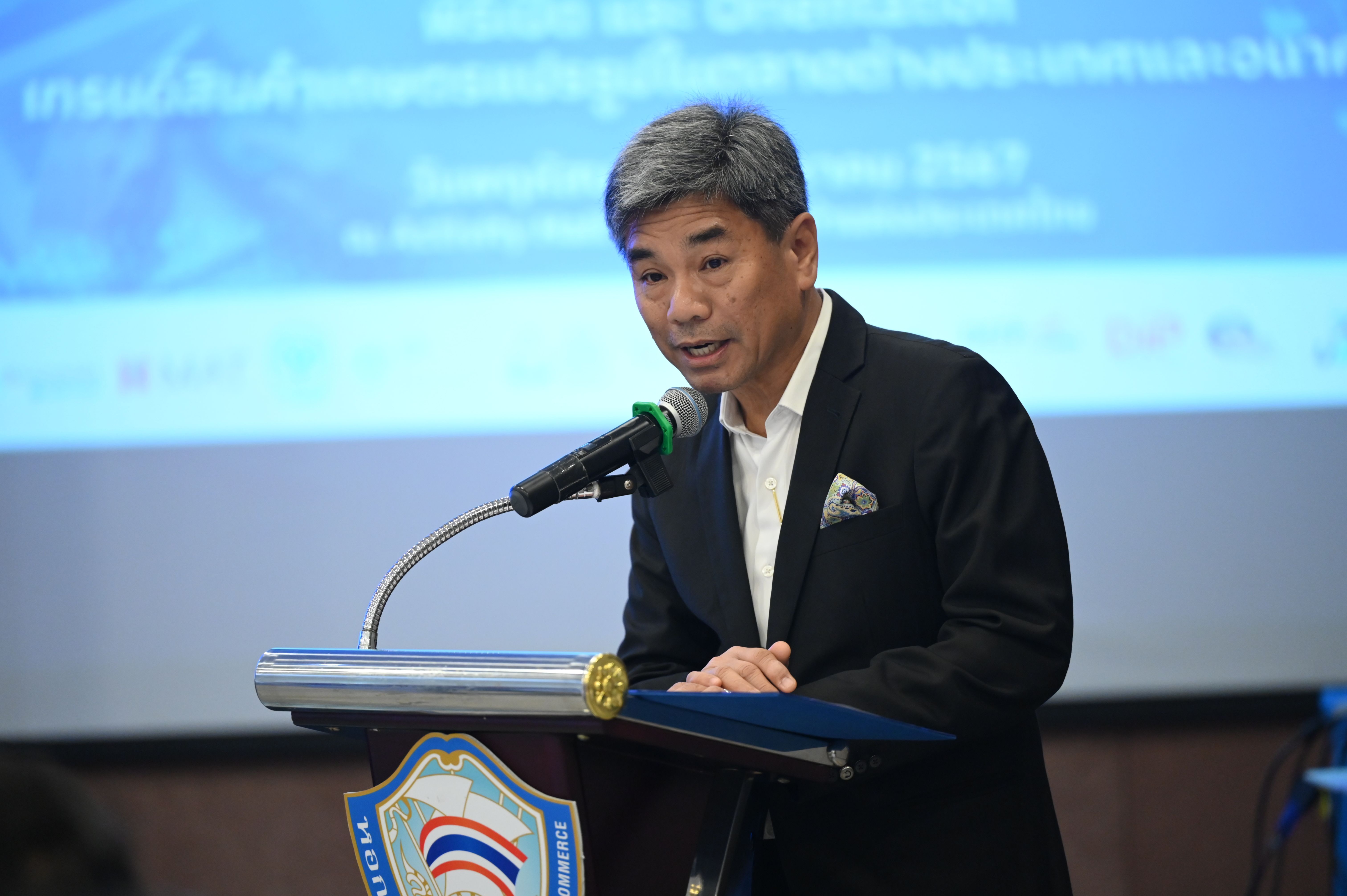 Asian man with grey hair speaking at a podium with a microphone.