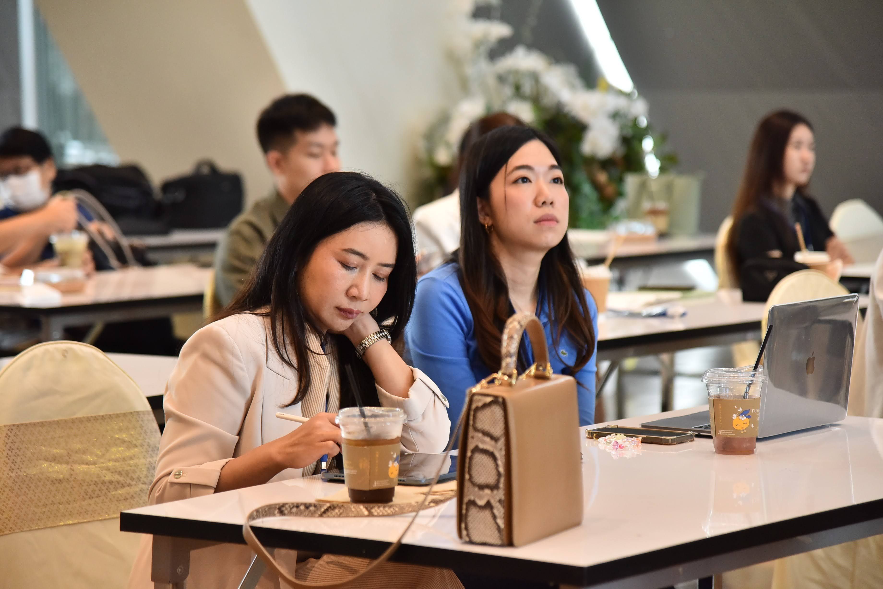 Two women, seminar attendees, listen attentively from their seats at a table.