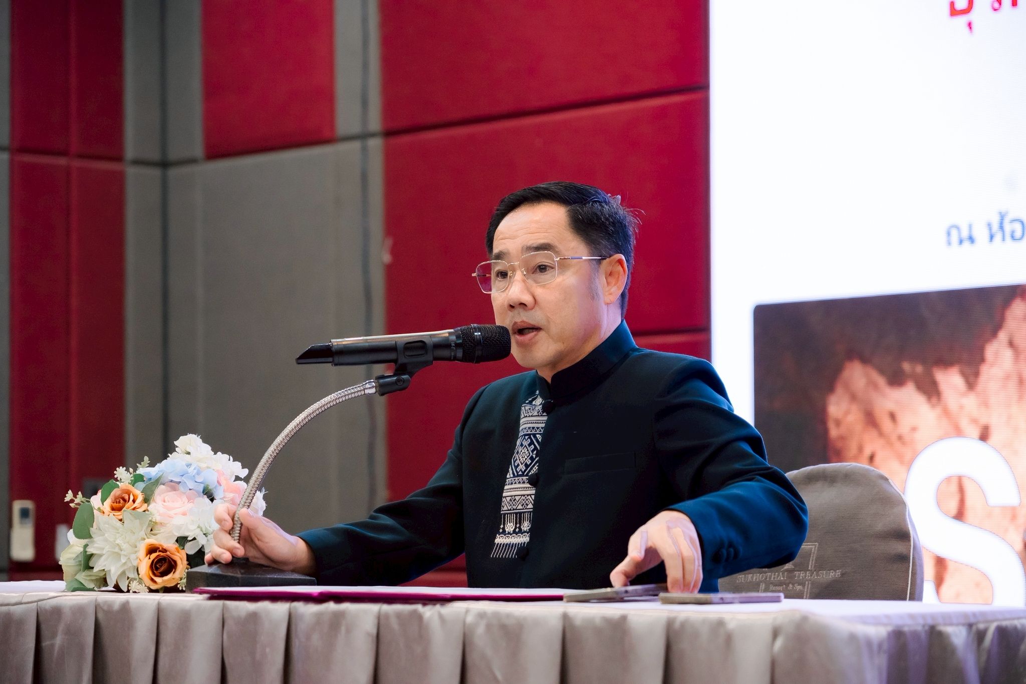 Man in glasses speaking into a microphone at a formal event.