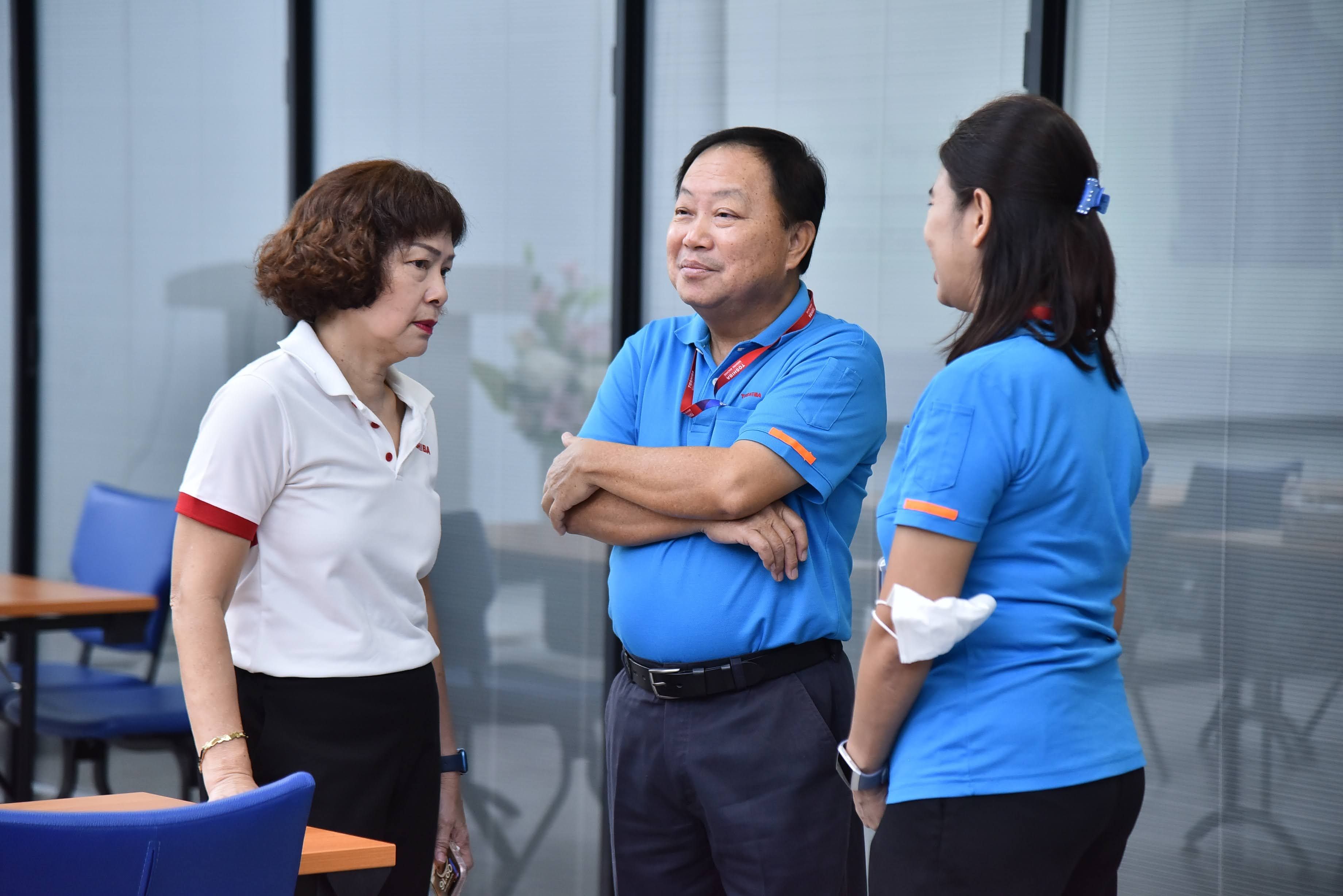 Three colleagues in polo shirts conversing casually in a modern office environment.