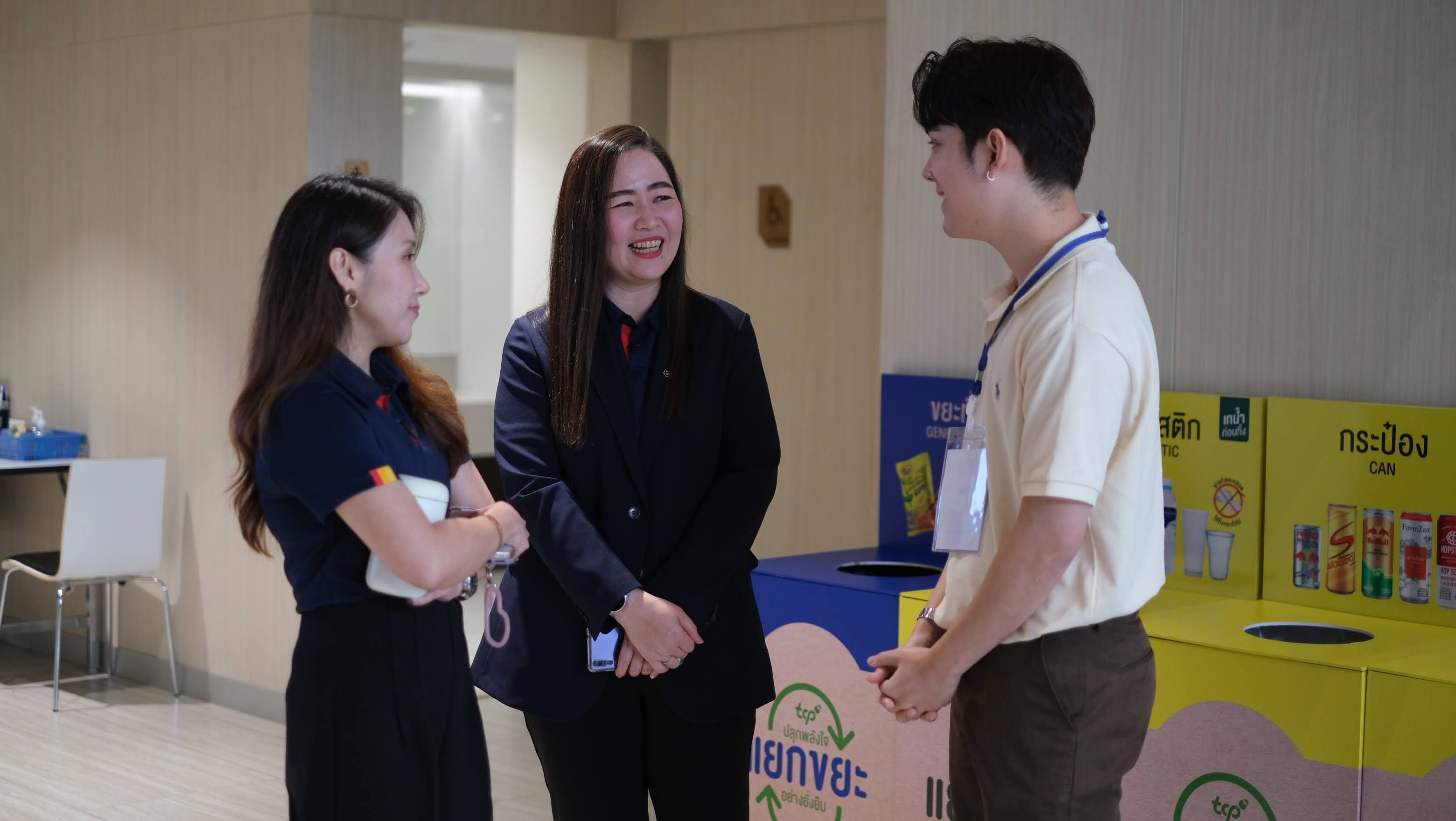Three people engaging in a friendly conversation near recycling bins.