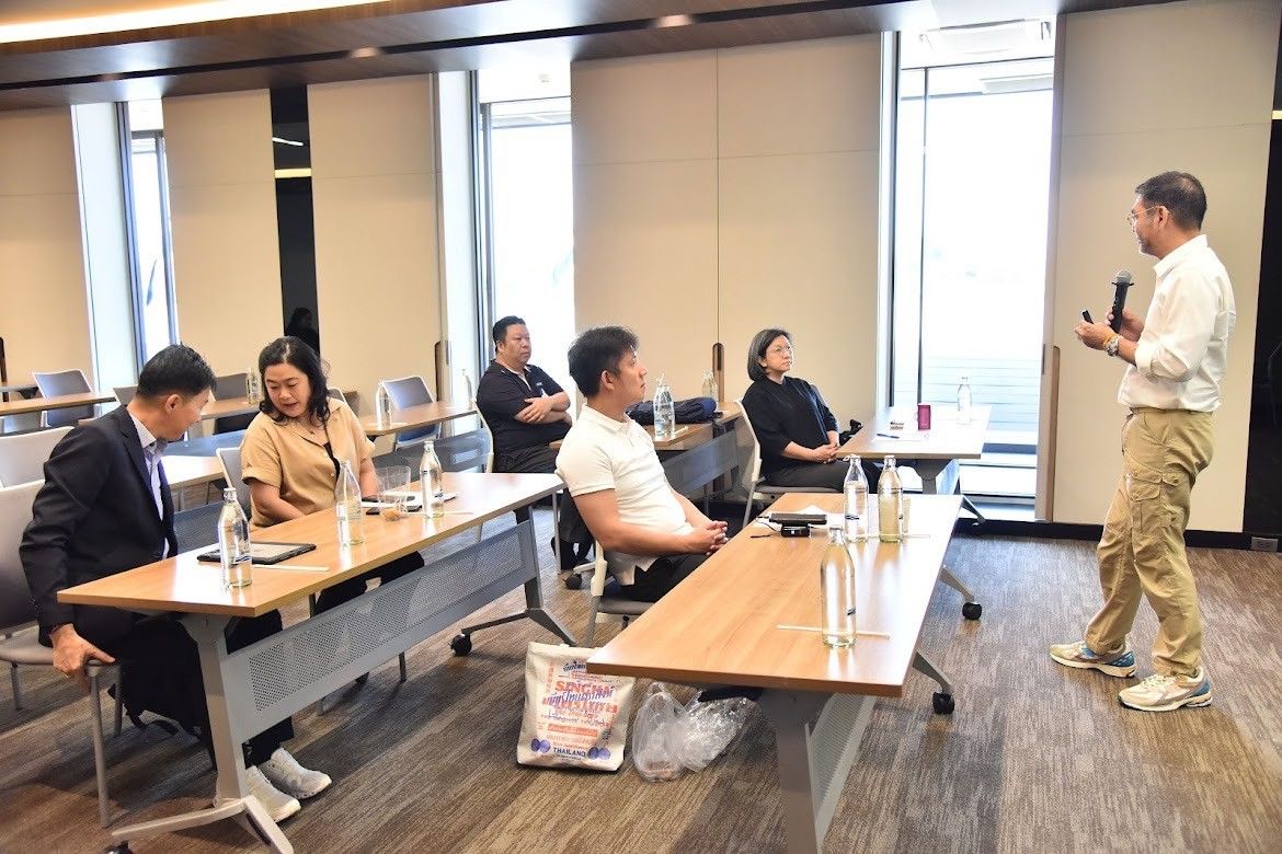 Man speaking to a small group of attendees in a modern conference room.