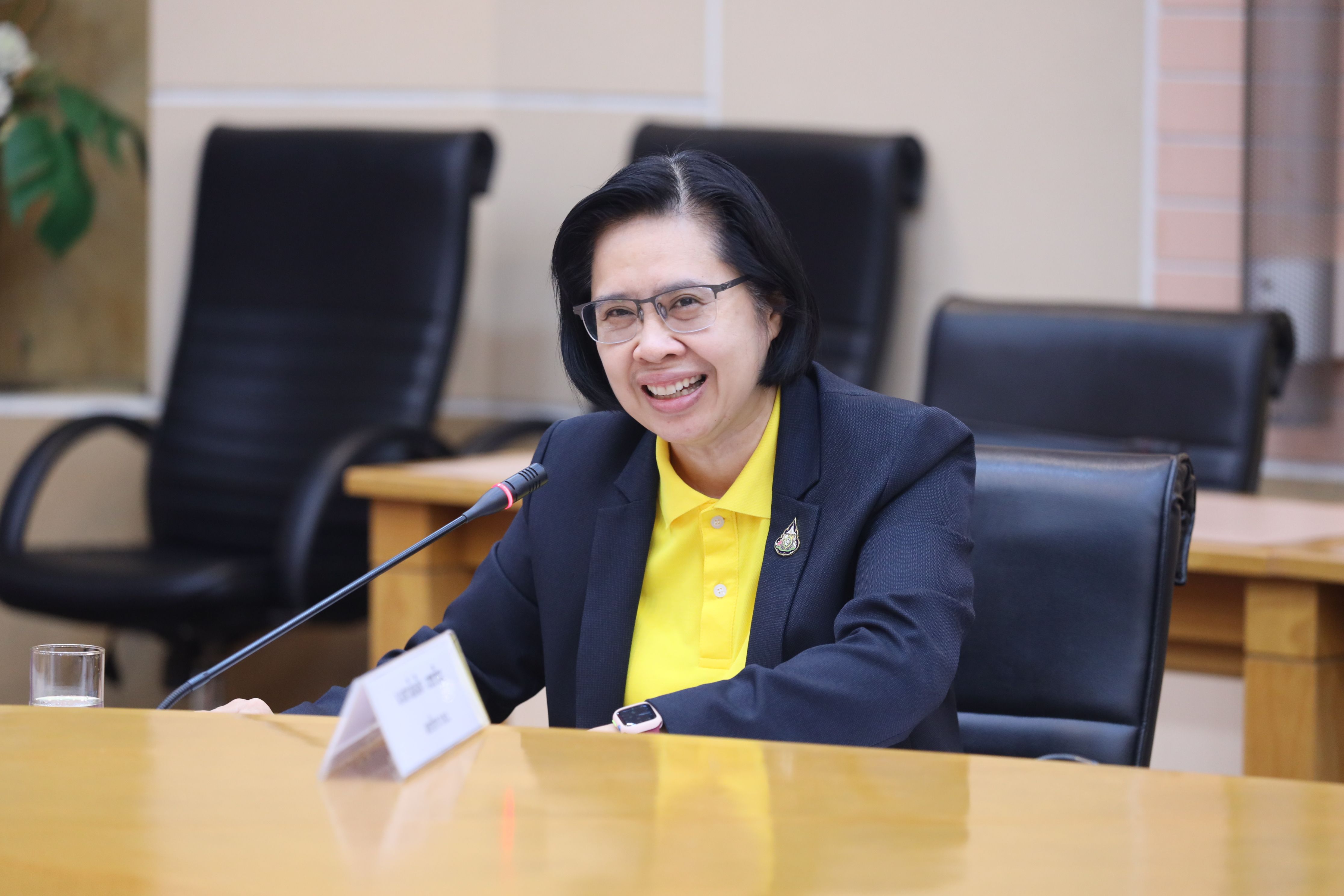 Smiling woman in glasses and yellow shirt sits at a conference table.