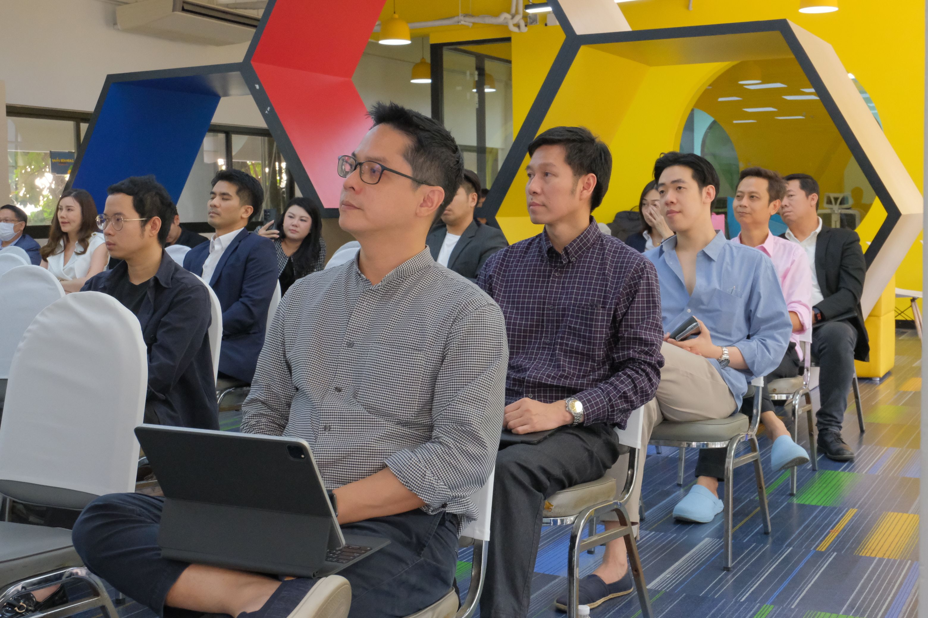 Professionals attend a conference, seated attentively with a laptop in a modern, colorful room.