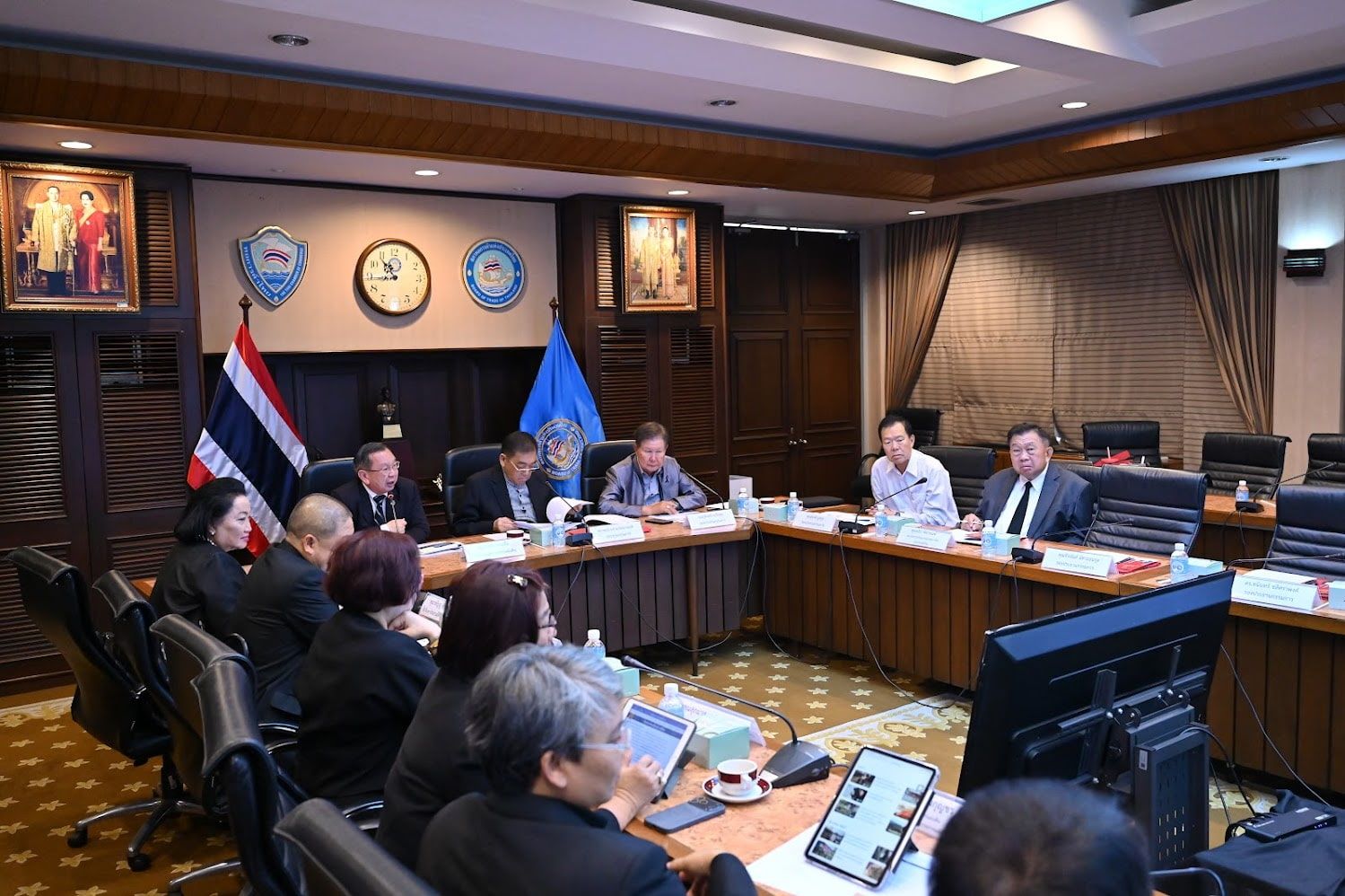Officials in a formal conference room attending a meeting with the Thai flag visible.