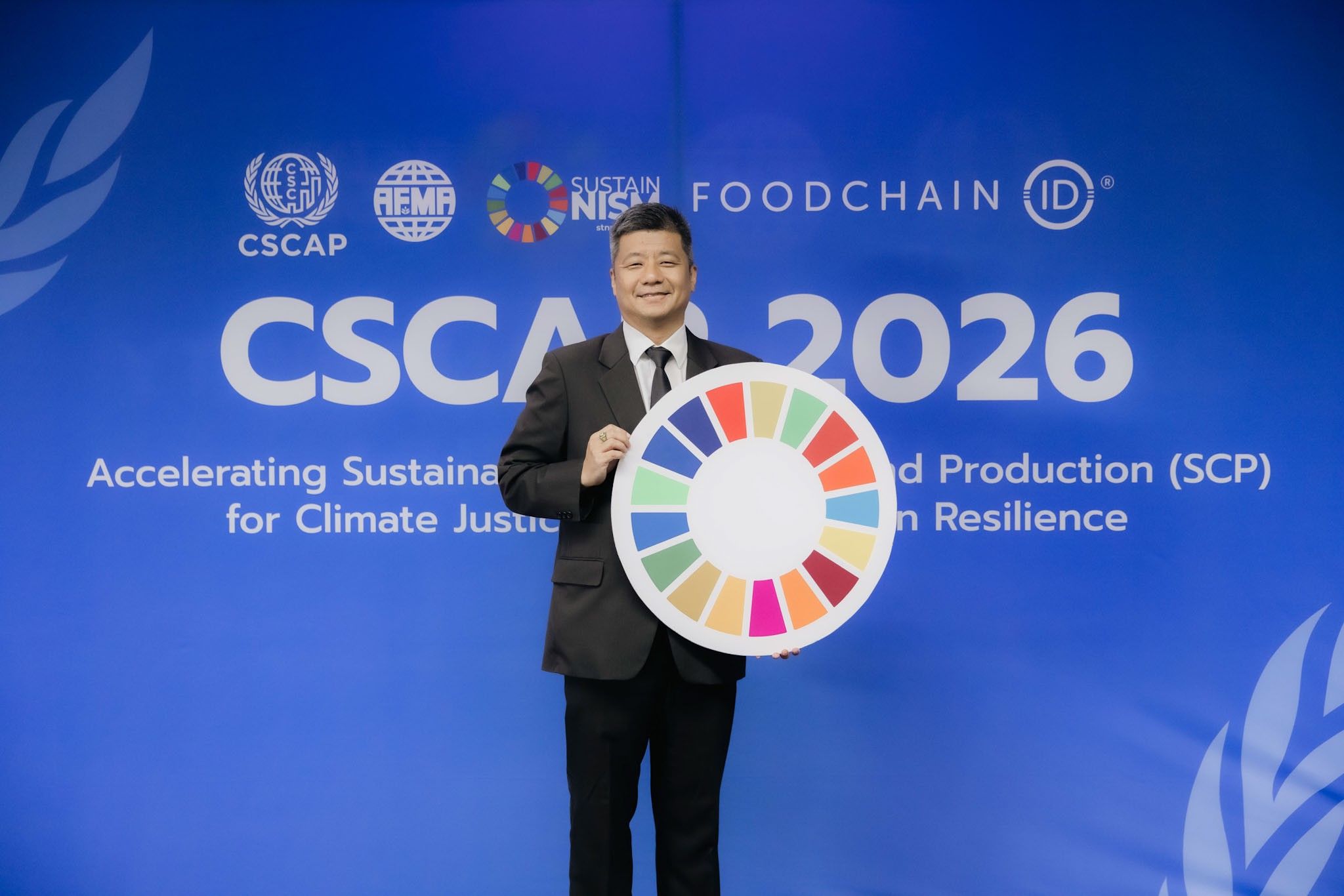 A man in a suit holds a colorful SDG emblem before a 'CSCA 2026' event backdrop.