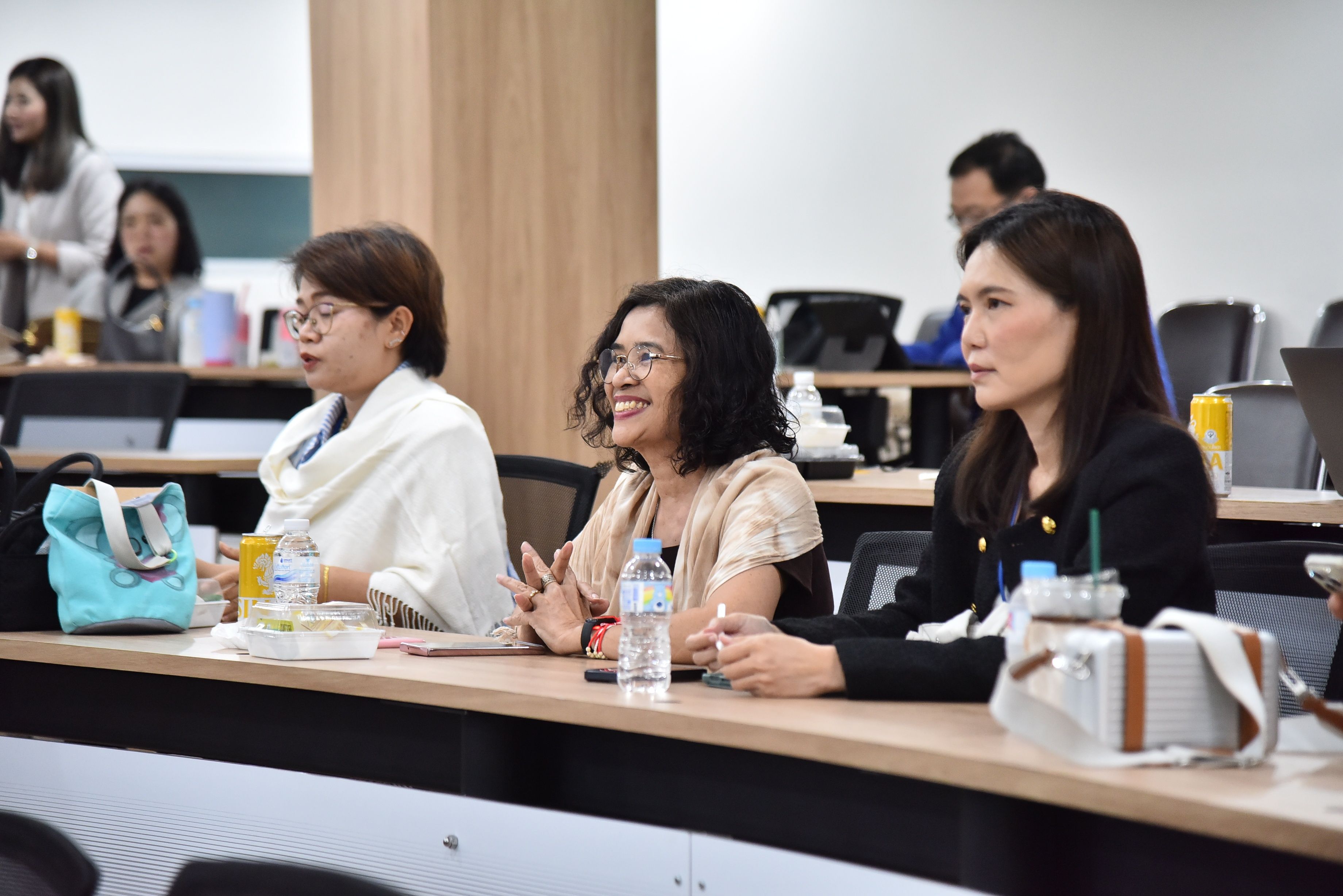 Three professional women actively participate in a meeting or class, one smiling brightly.