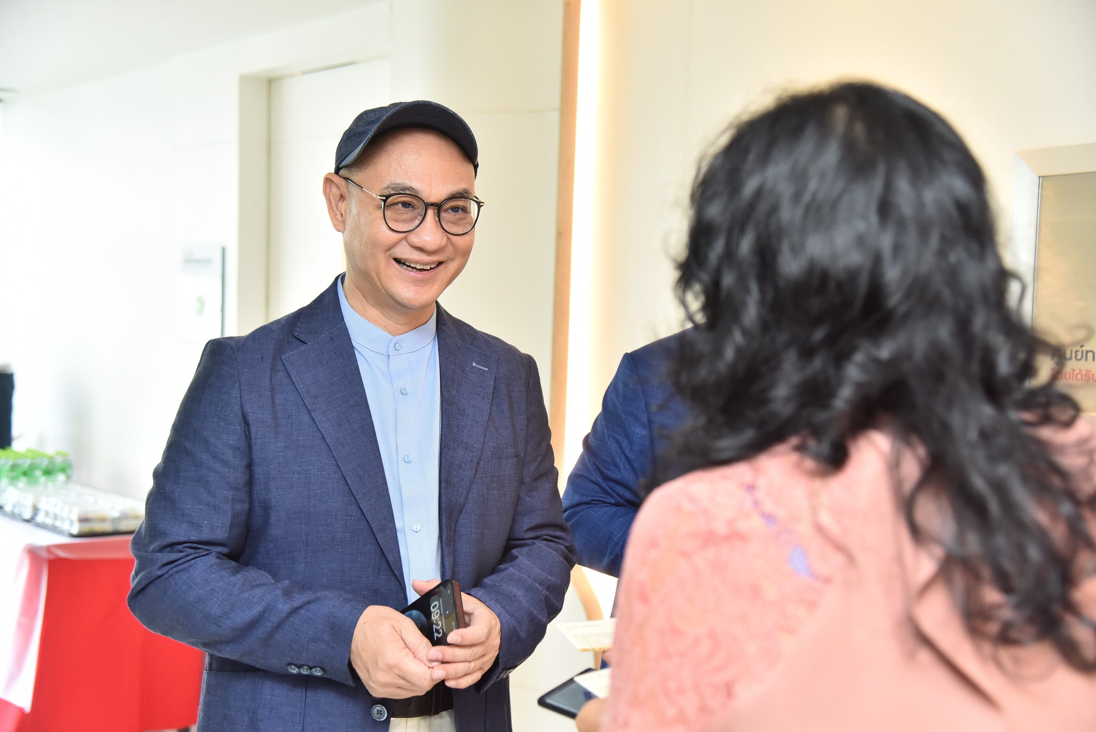 Man in blue jacket and cap smiling while talking to another person.