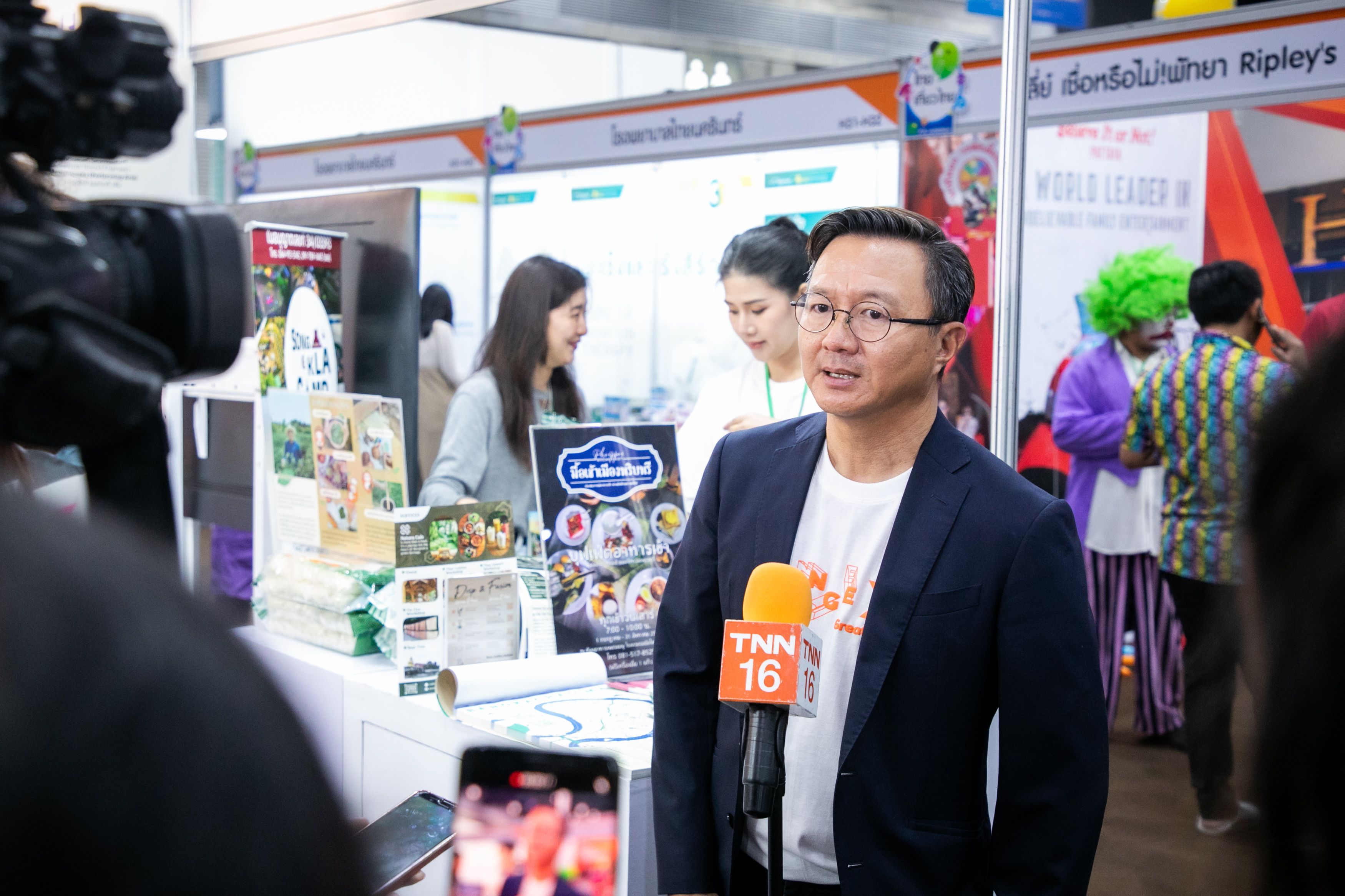 Man in glasses and blazer speaks into a TNN 16 microphone at an event.