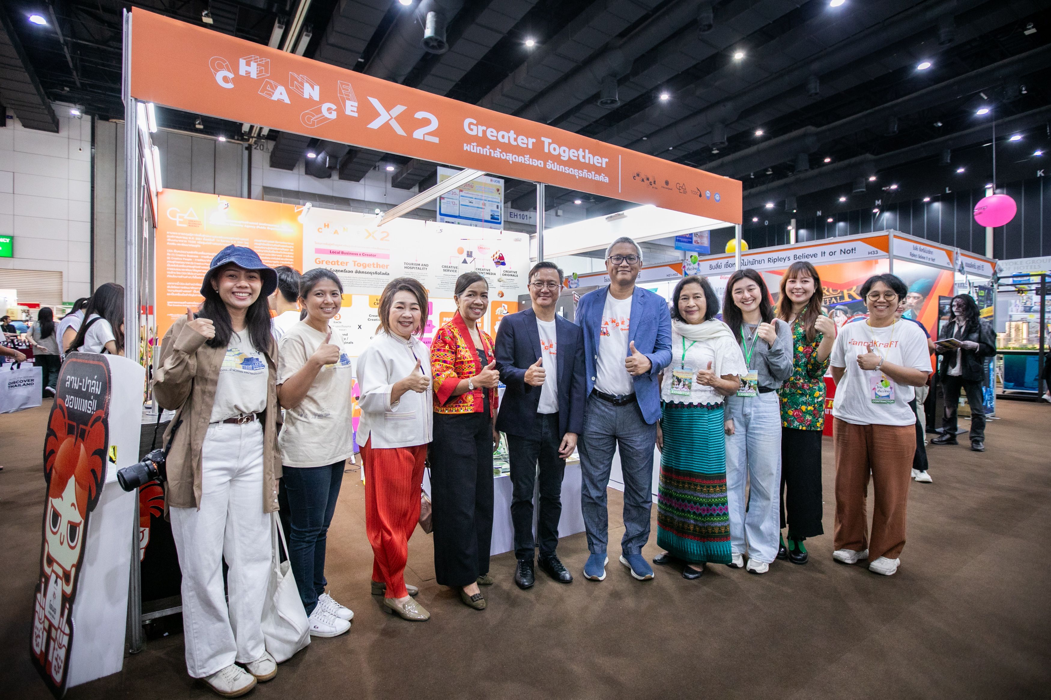 Diverse group smiling and giving thumbs up at a chanchax2 Greater Together exhibition booth.