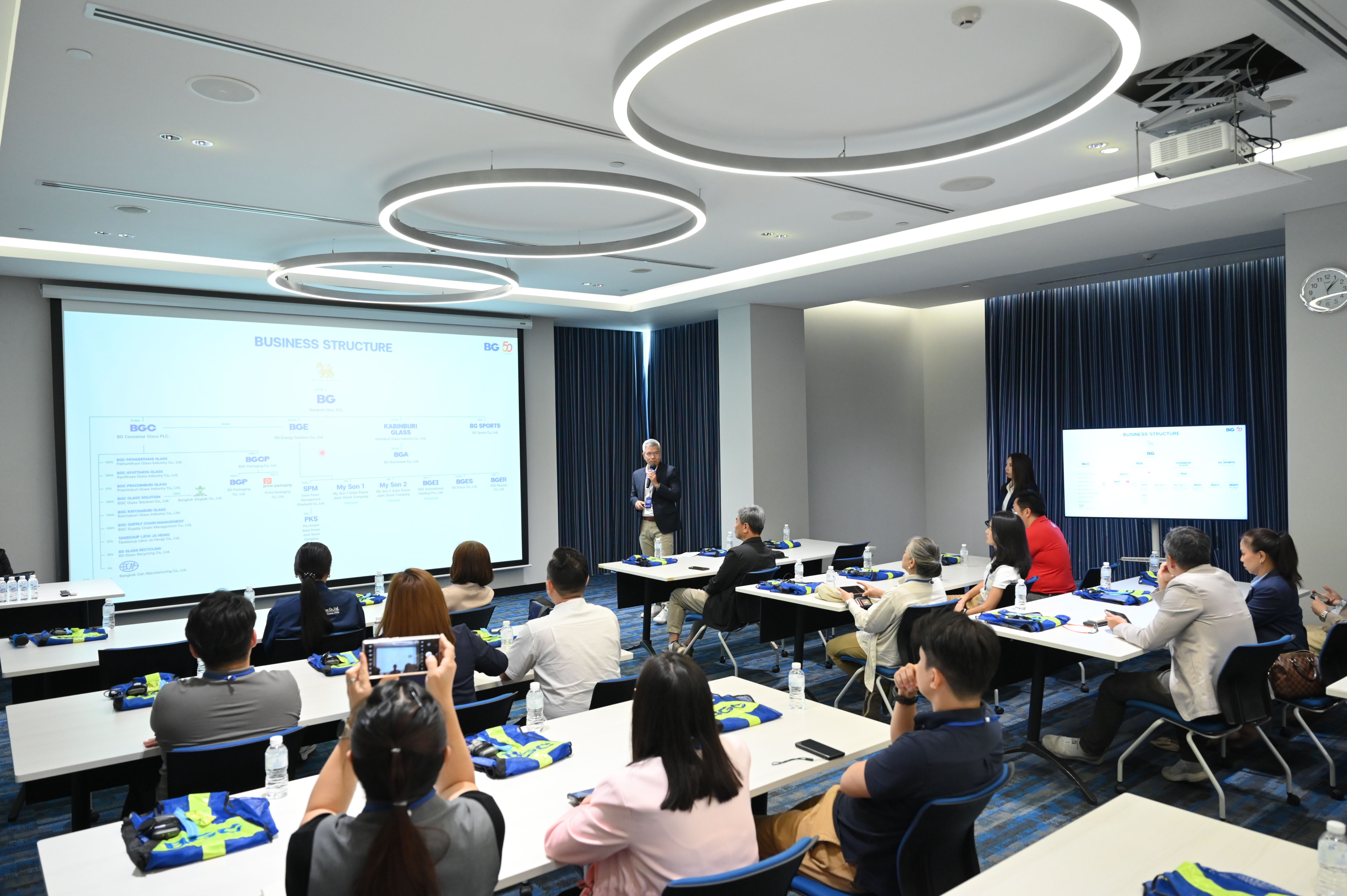 Speaker presenting on a large screen to an audience seated in a modern conference room.