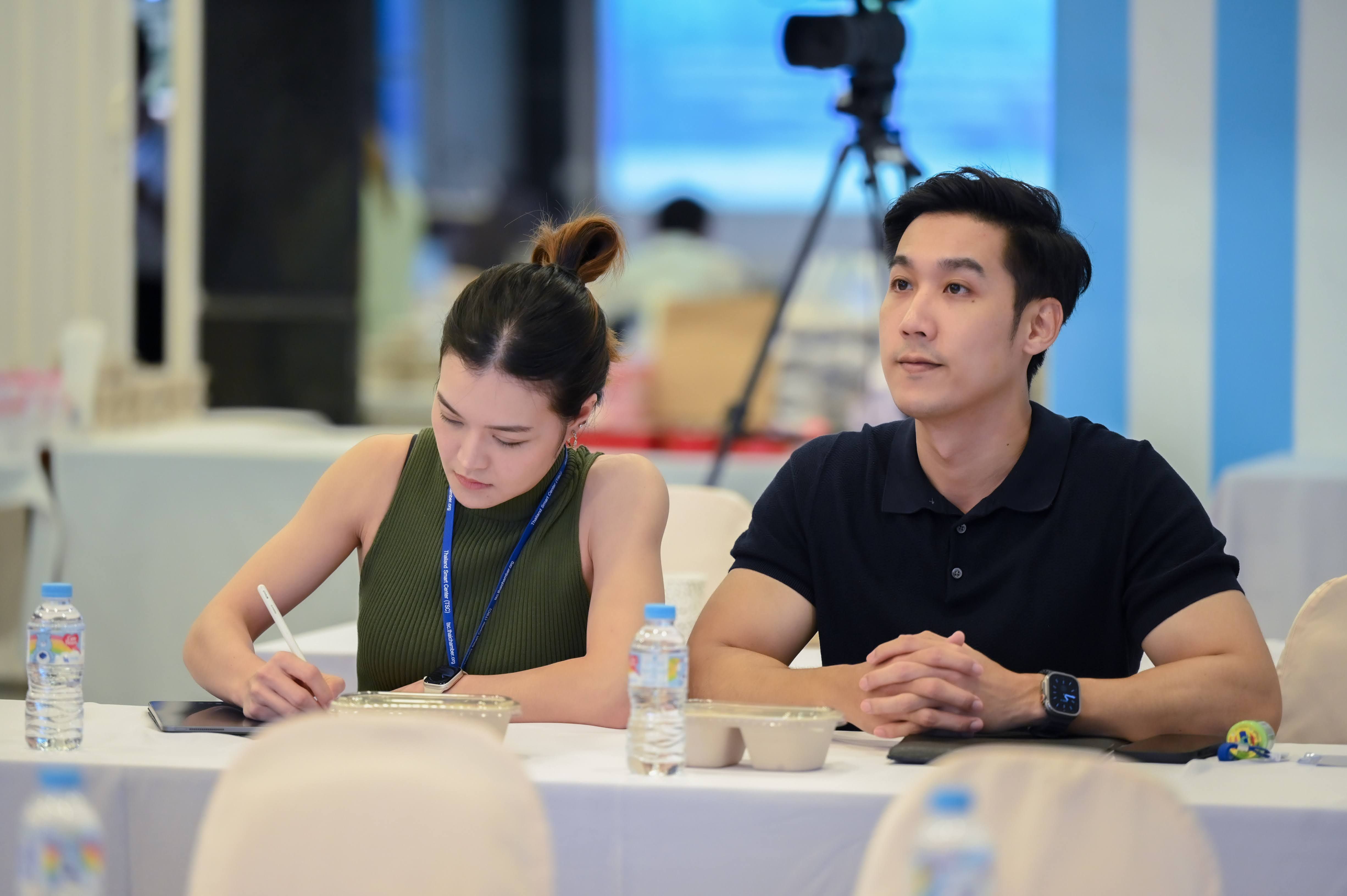 A woman writes notes while a man listens attentively at a professional conference.