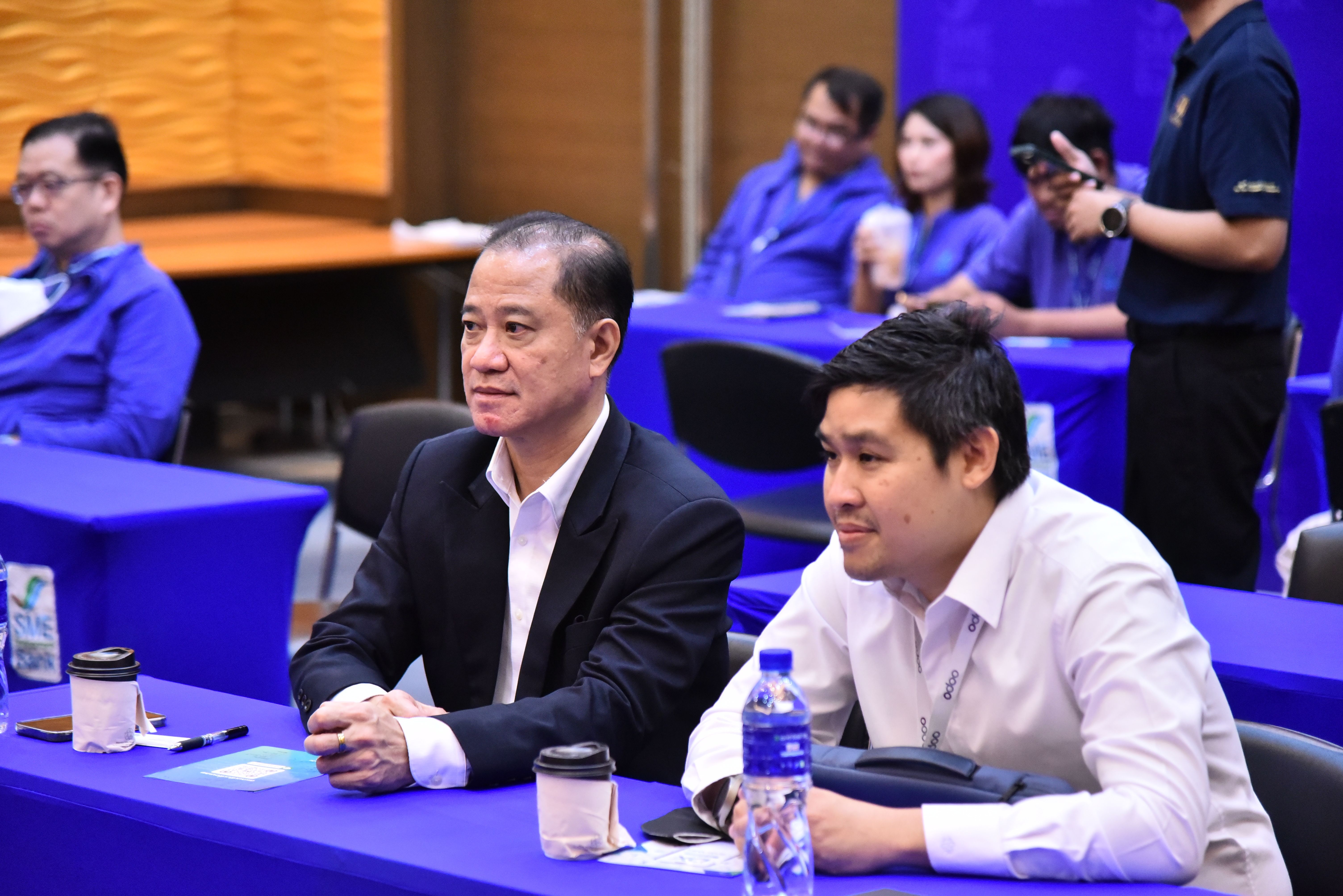 Two men attentively seated at a blue table during a conference event.
