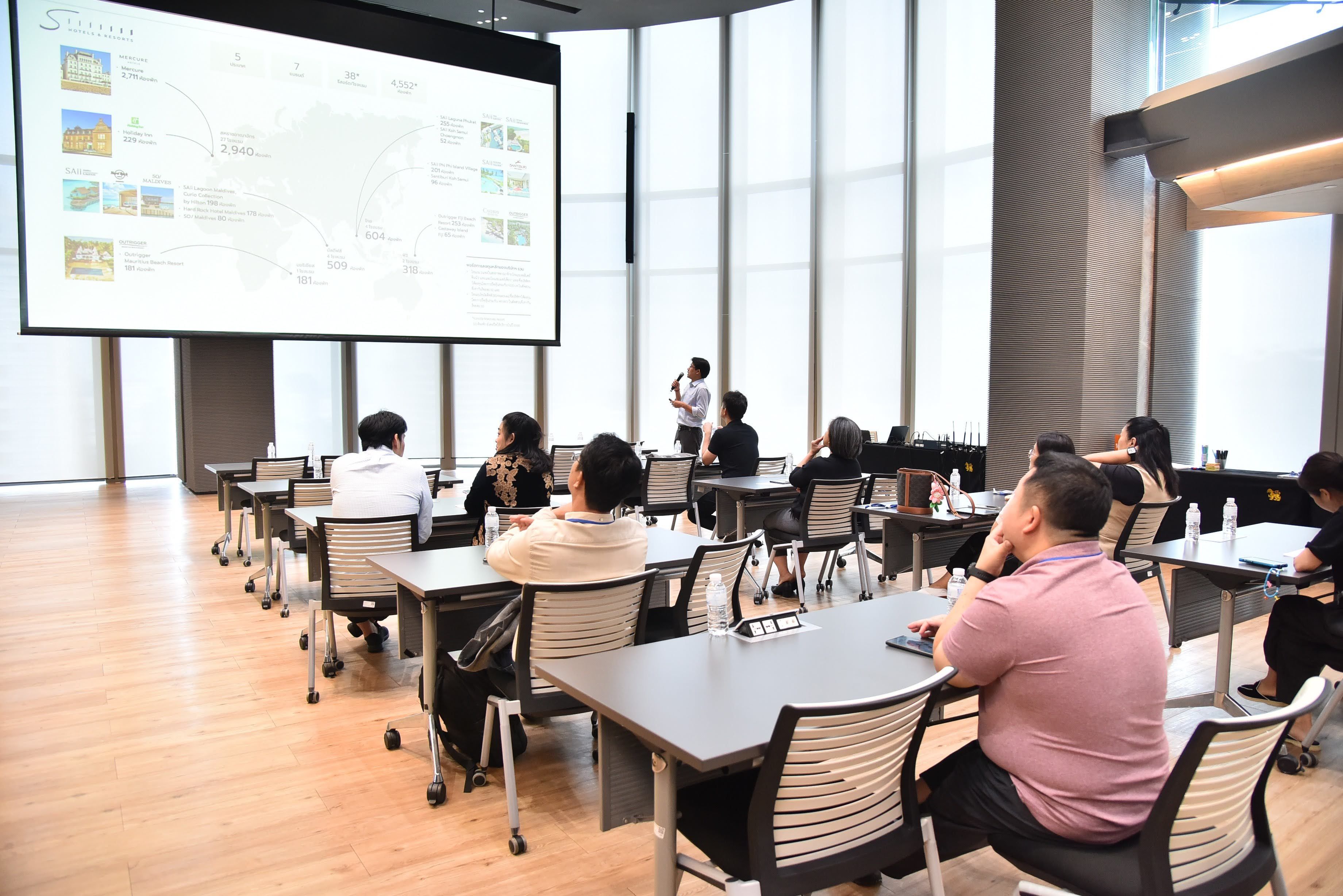 Attendees watch a presentation on a large screen in a modern, bright conference room.