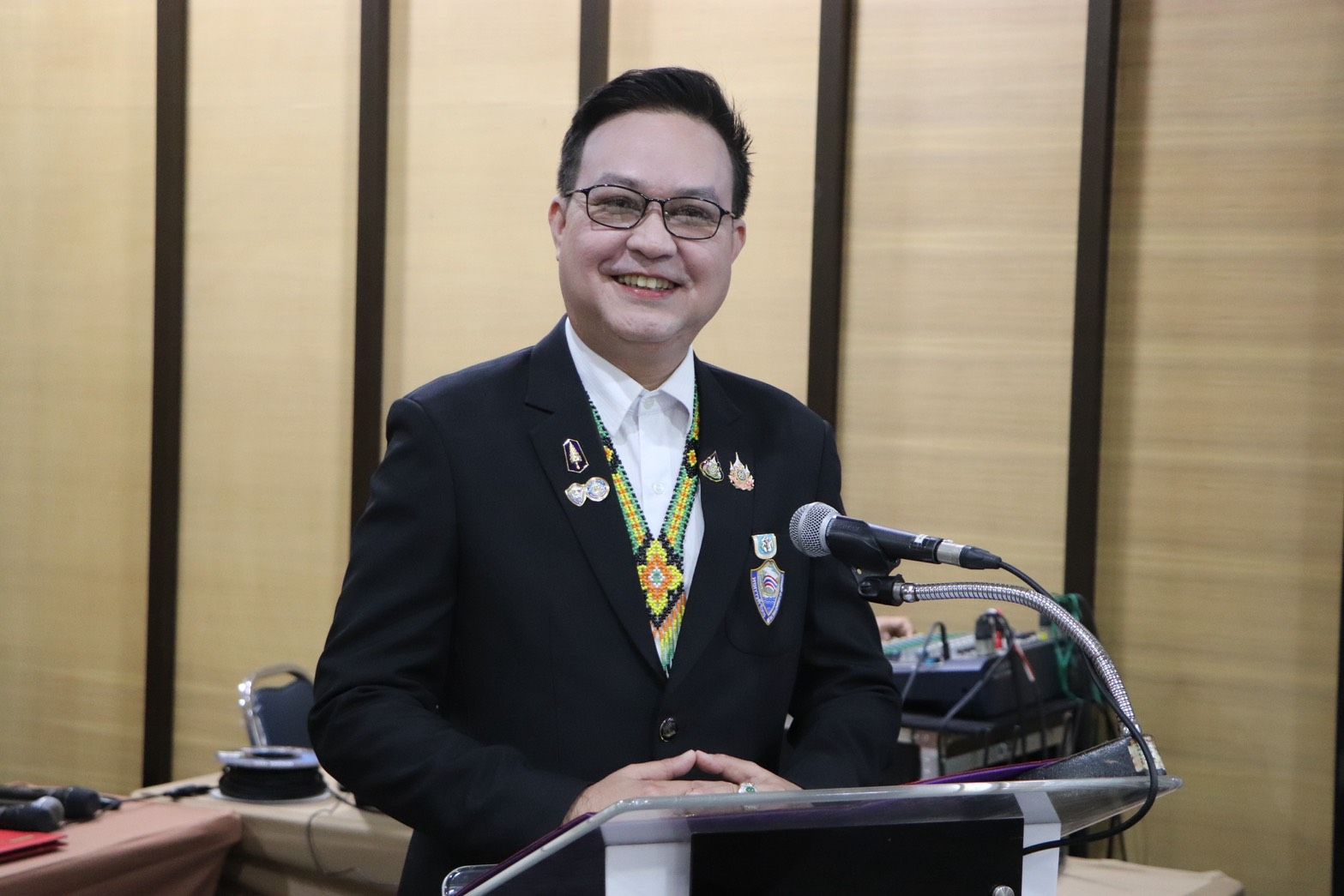 Smiling man in a dark suit with medals standing at a podium.