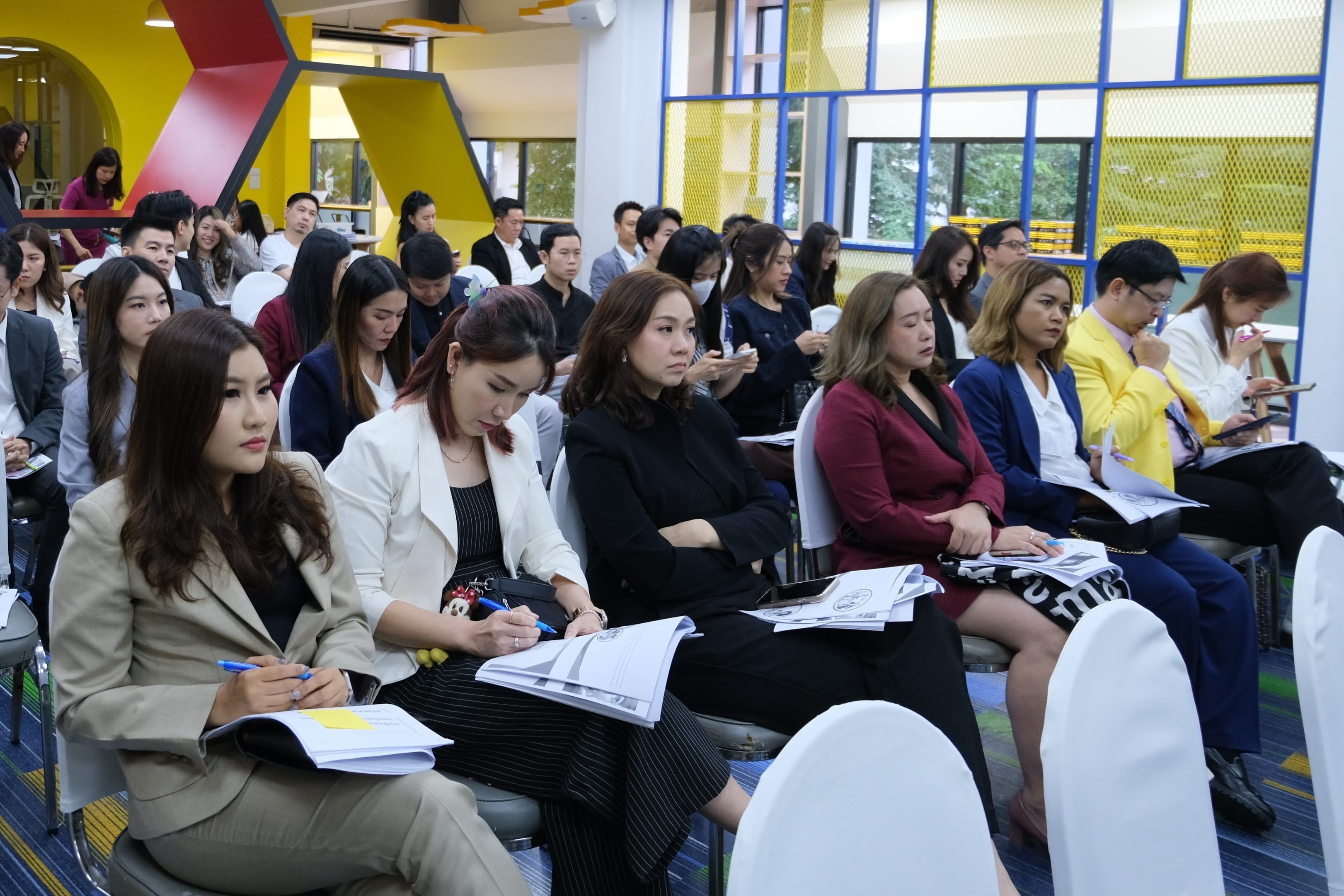 A group of professionals, mostly women, attentively seated in rows during a conference or seminar.