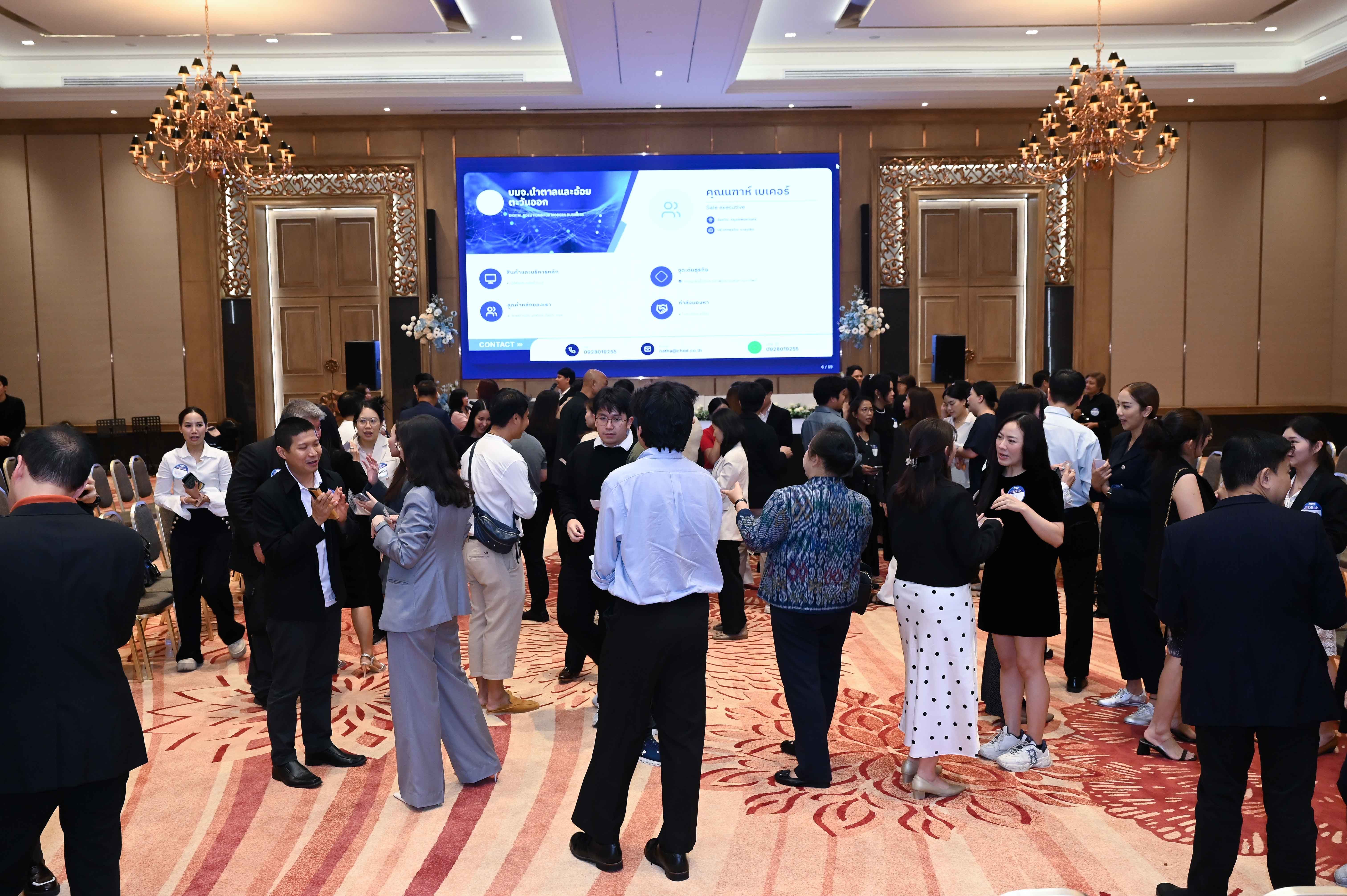 A large group of people networking in a spacious conference hall with a bright presentation screen.