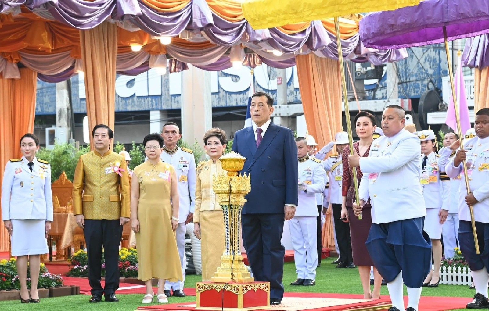 A group of formally dressed officials attend a ceremony with a golden pedestal.