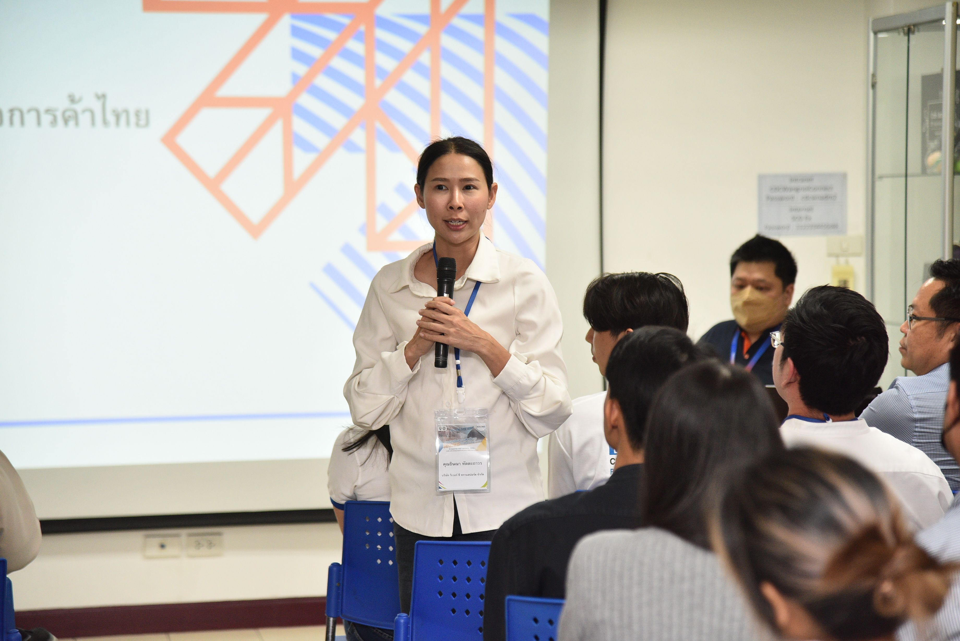 Woman speaking into microphone presenting to an audience at a conference.