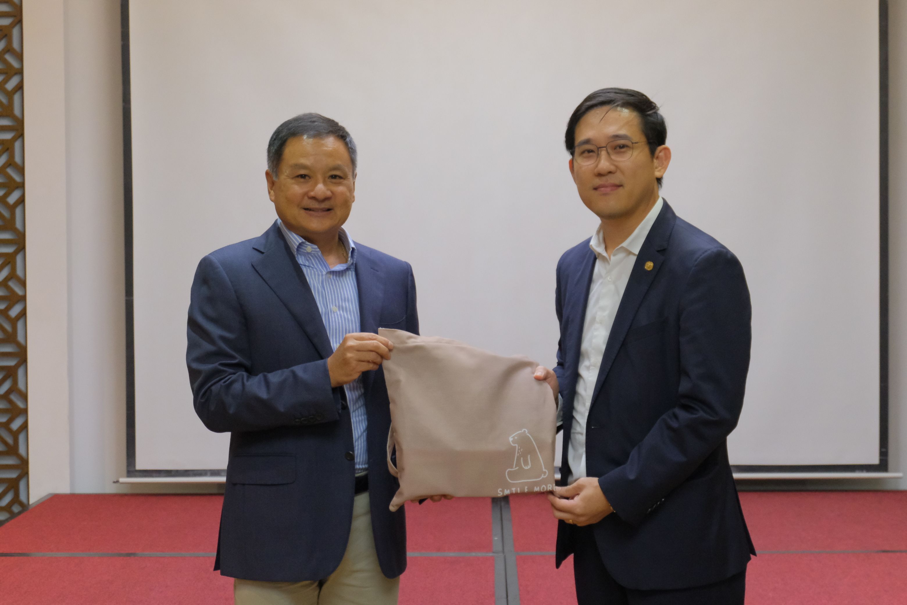 Two smartly dressed men smiling, one presents a small gift bag to the other.