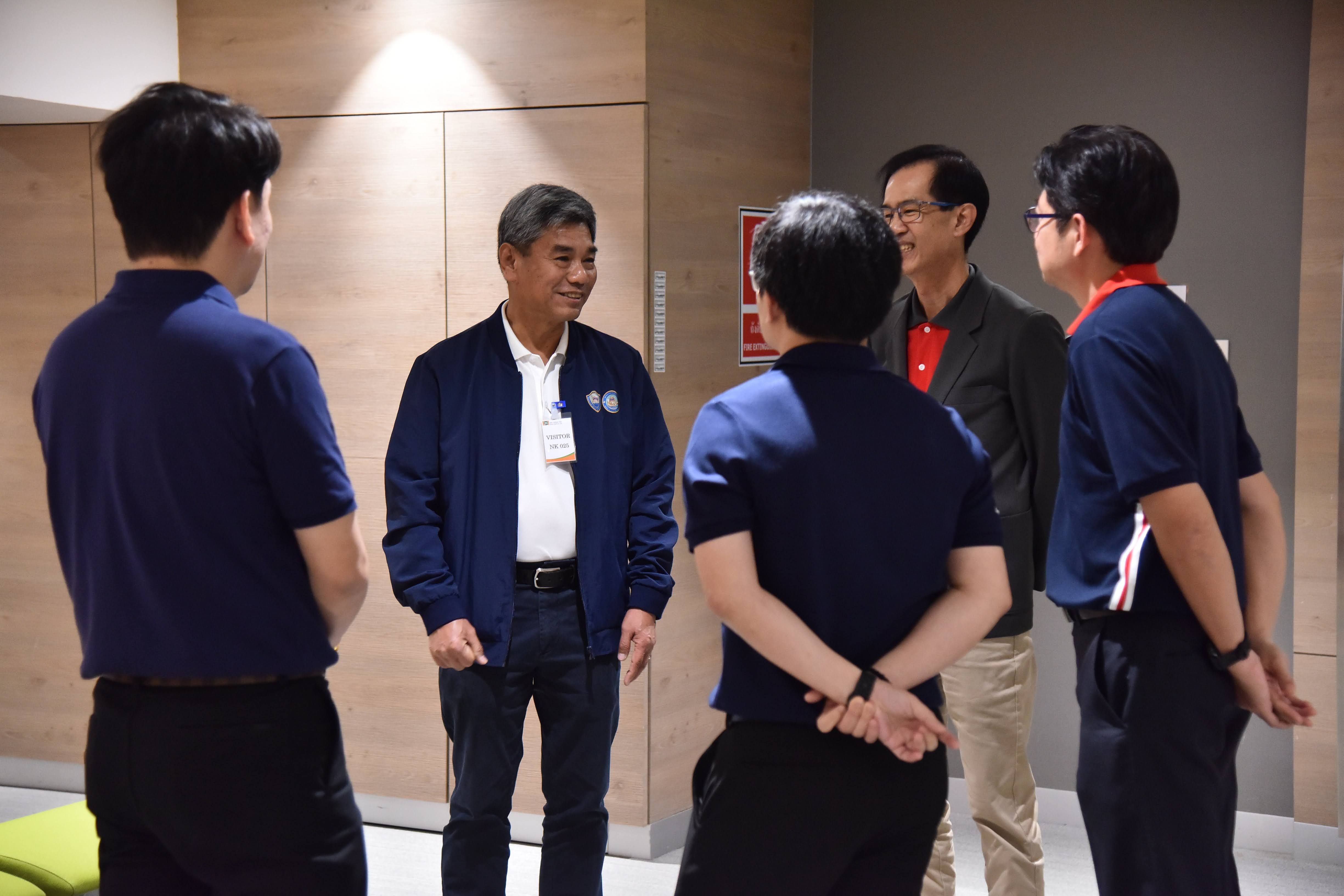 Five men converse in a modern office, an older man smiles at his colleagues.